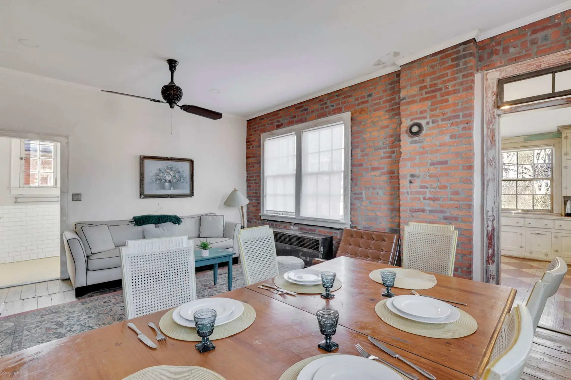 A dining table is set for a meal in front of a brick wall and a window.