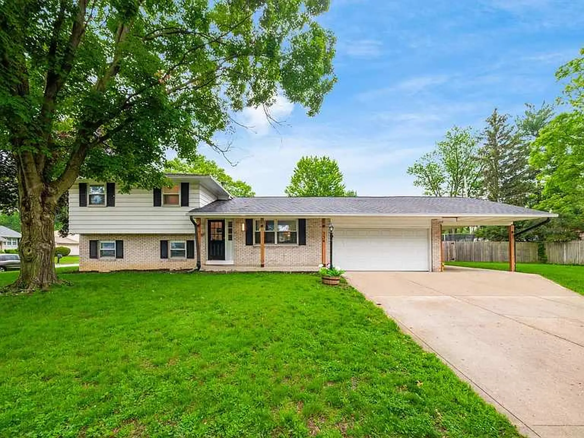 A ranch-style home with a covered carport, situated on a grassy lawn.
