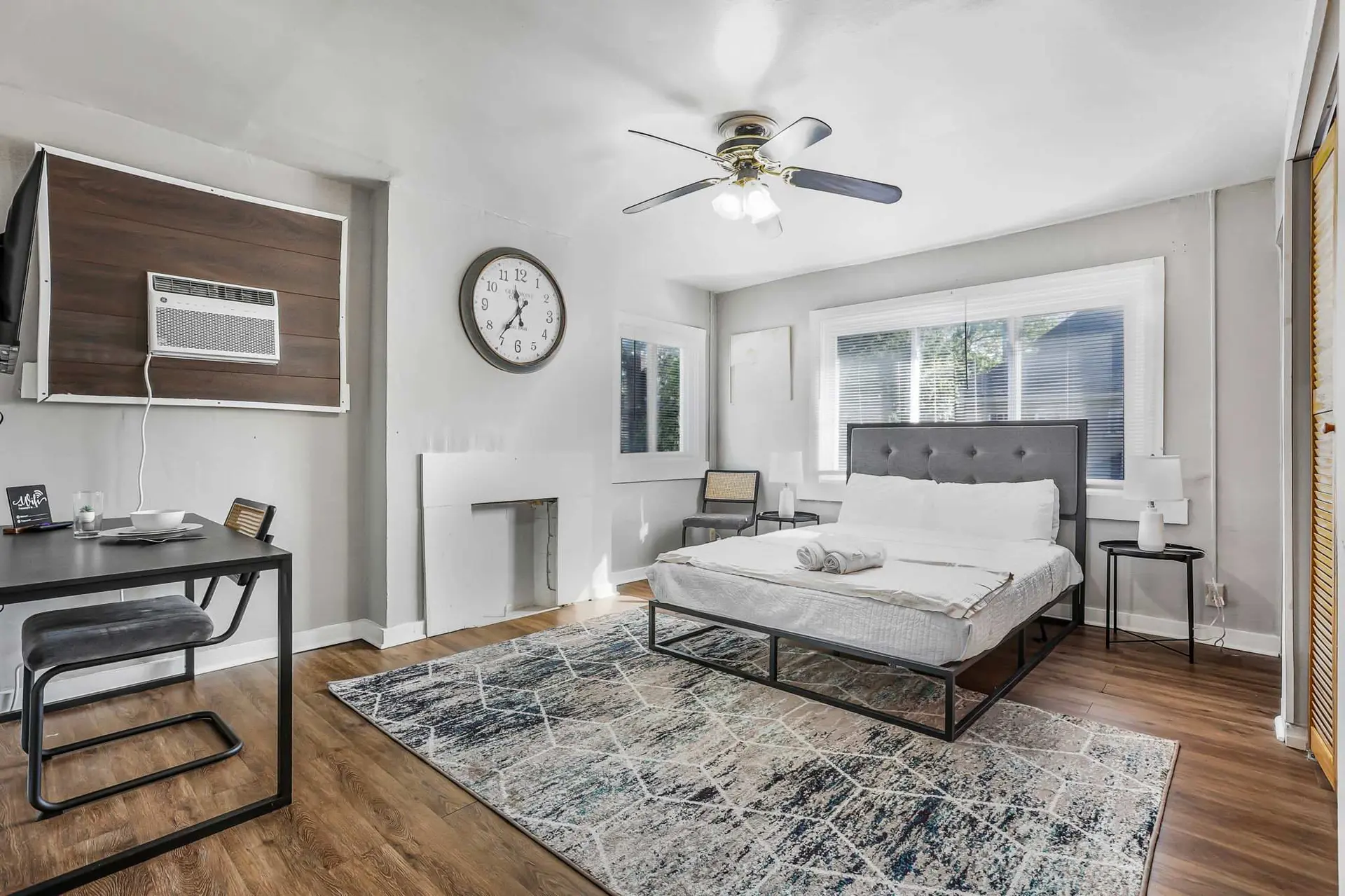 A bedroom with a bed, dining table, and air conditioner.