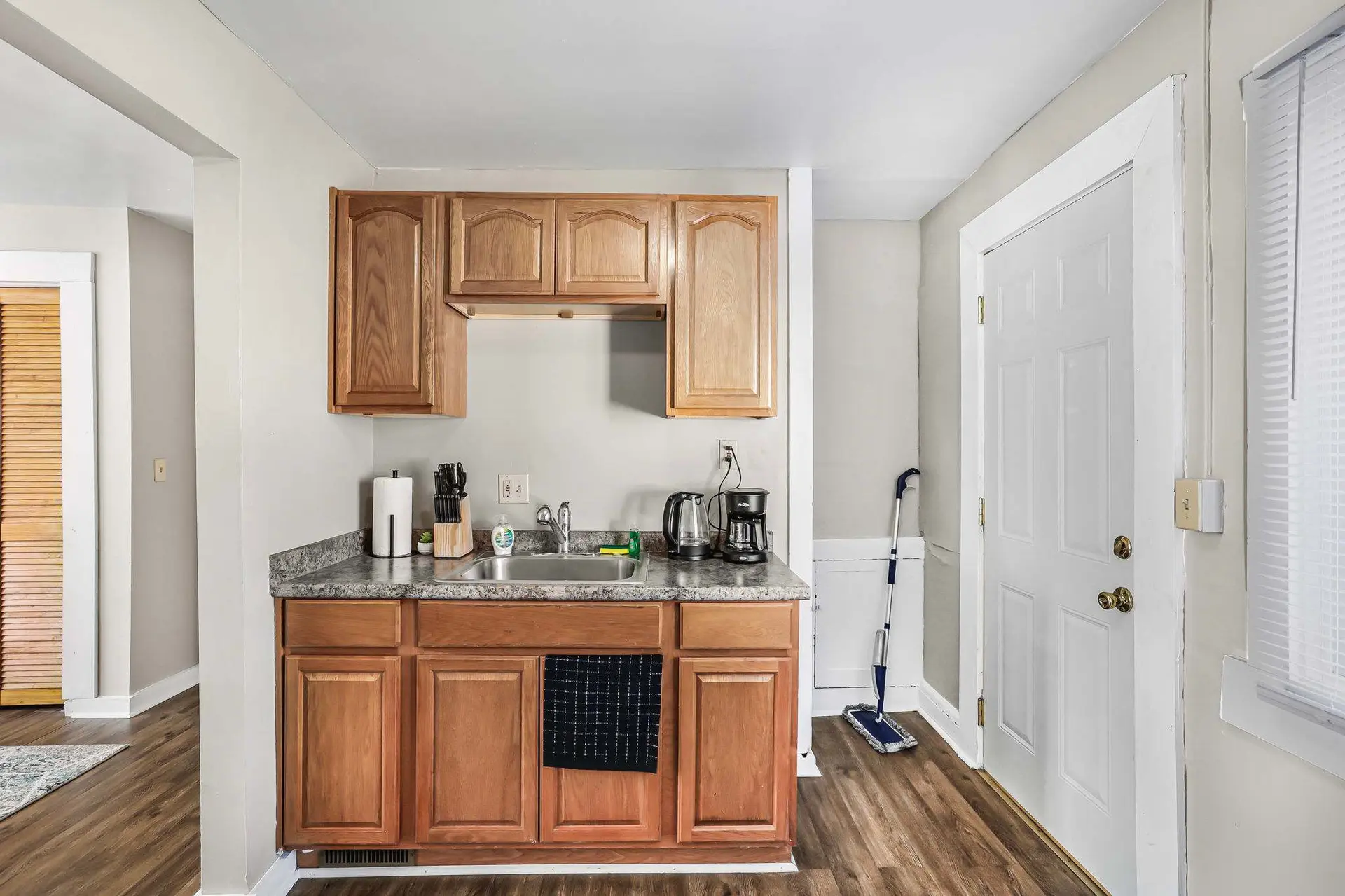 Kitchen area with wooden cabinets, sink, coffee maker, and a mop.
