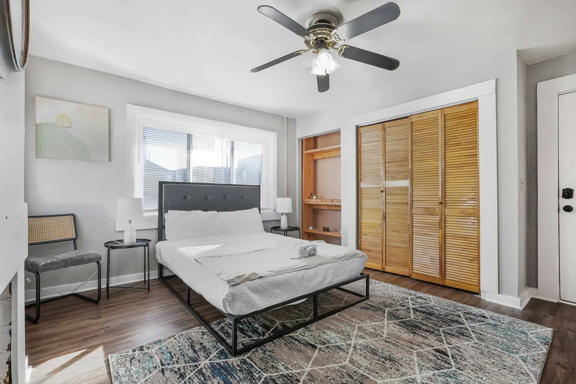 A bedroom with a bed, closet, ceiling fan, and artwork.