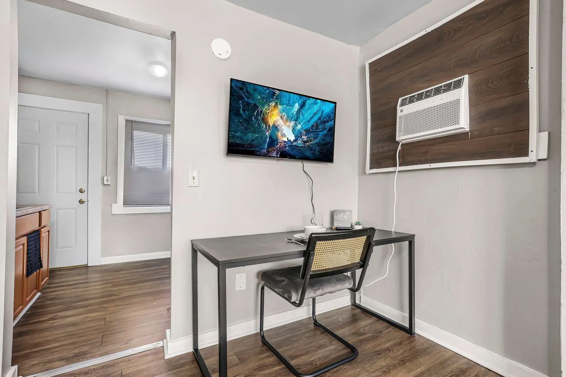A desk with a chair sits in front of a TV in a room with wood floors and a window.