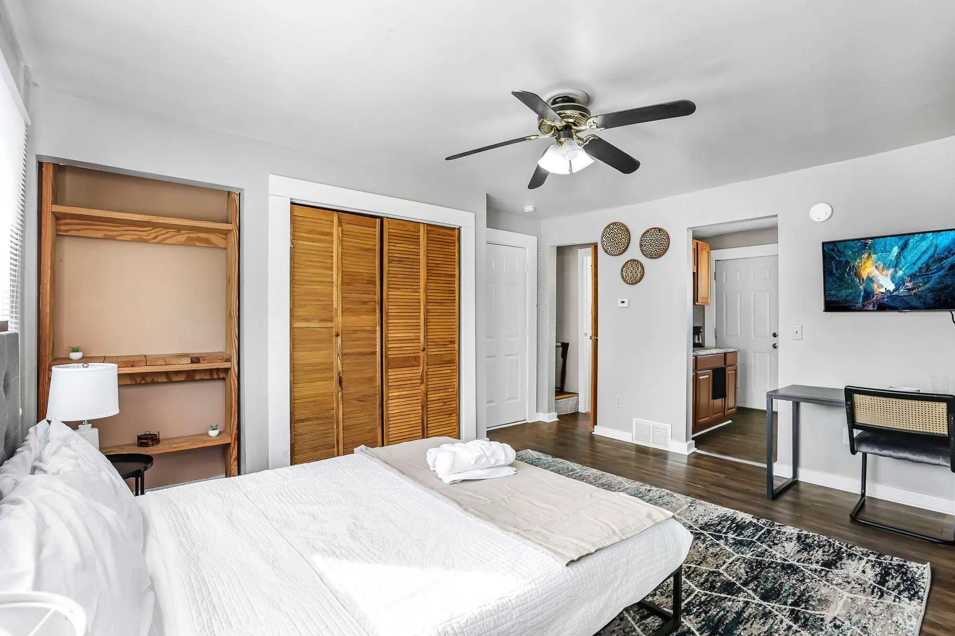 A modern bedroom with a bed, wooden closets, a TV, and a ceiling fan.