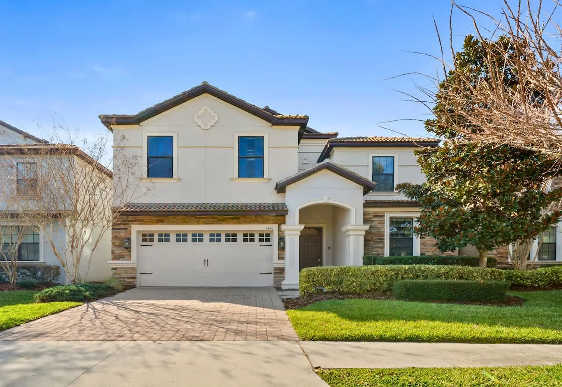 A two-story beige house with a white garage door and arched entrance.