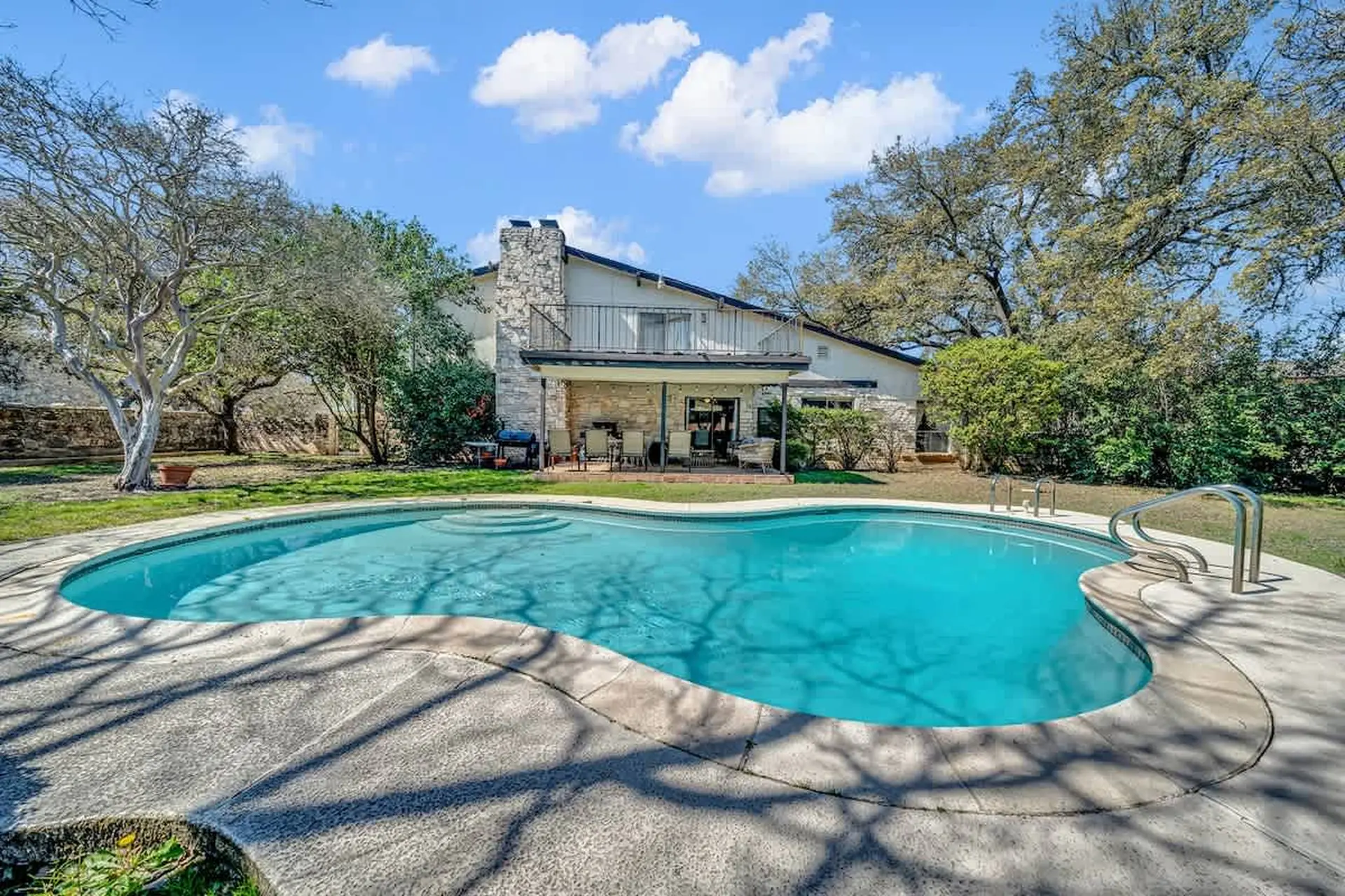 A backyard with a swimming pool and a house featuring a stone chimney.