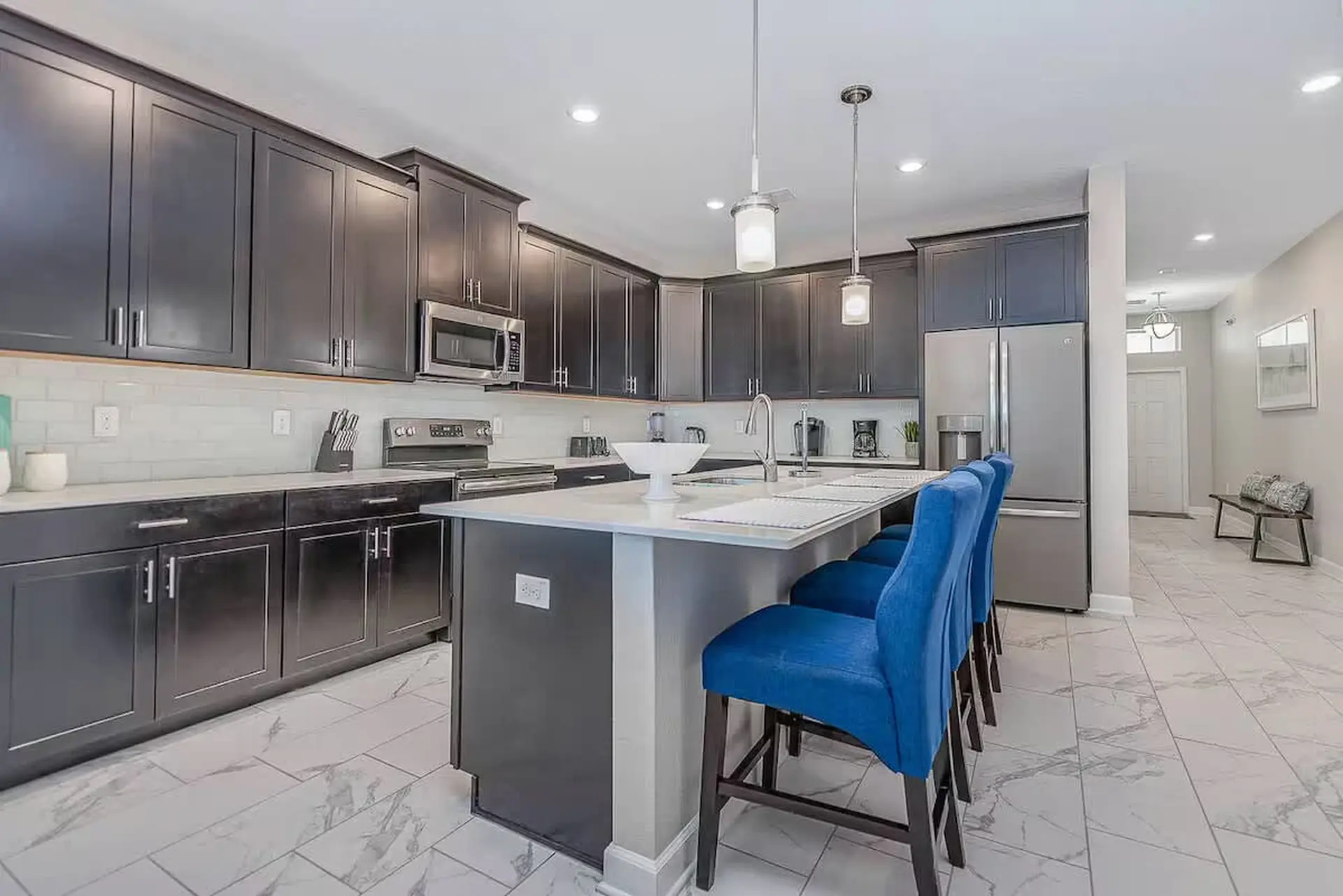 A modern kitchen with dark cabinets, a white island with blue bar stools, and stainless steel applia