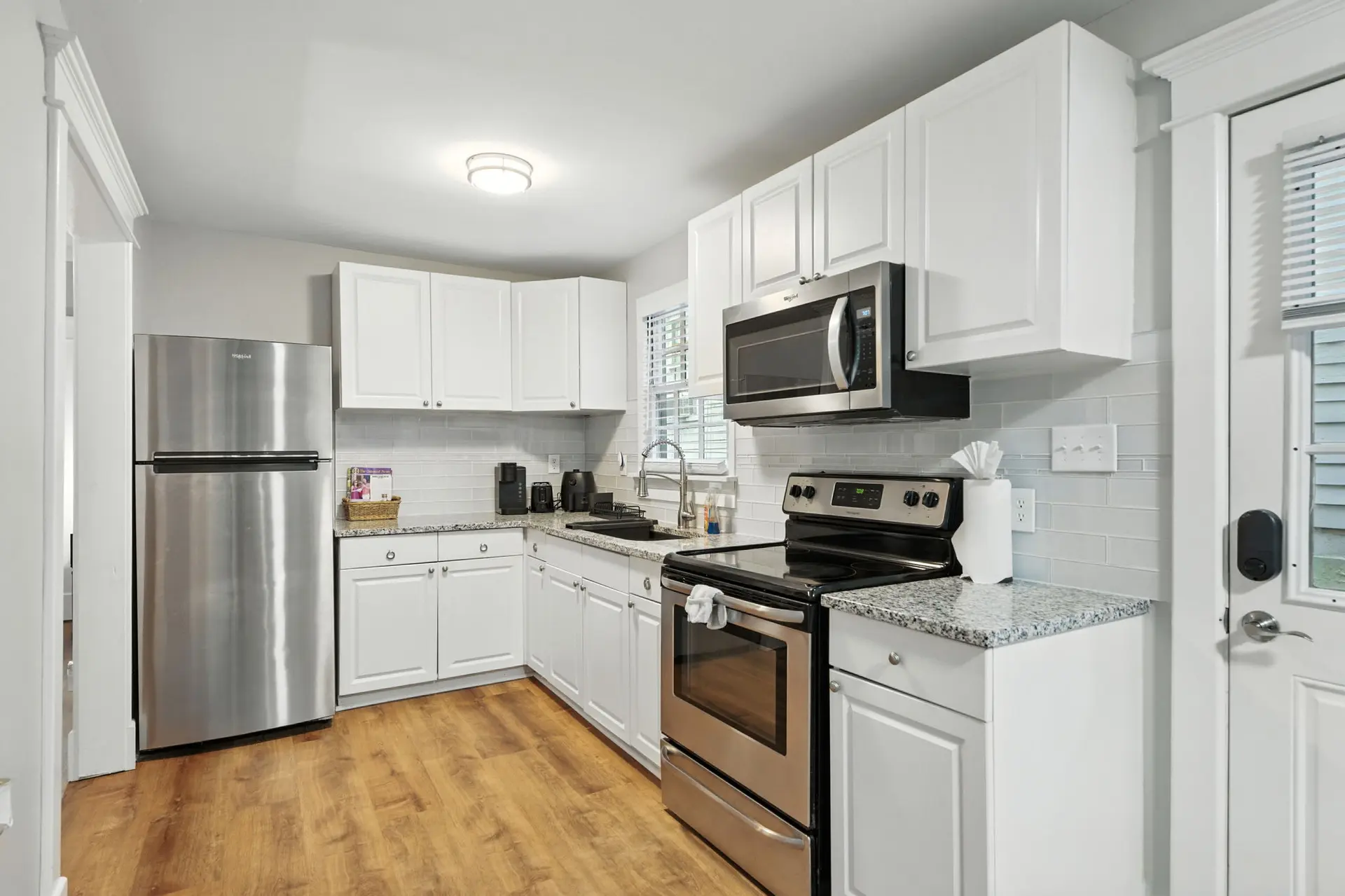 A stainless steel refrigerator, white cabinets, and a white subway tile backsplash are featured in t
