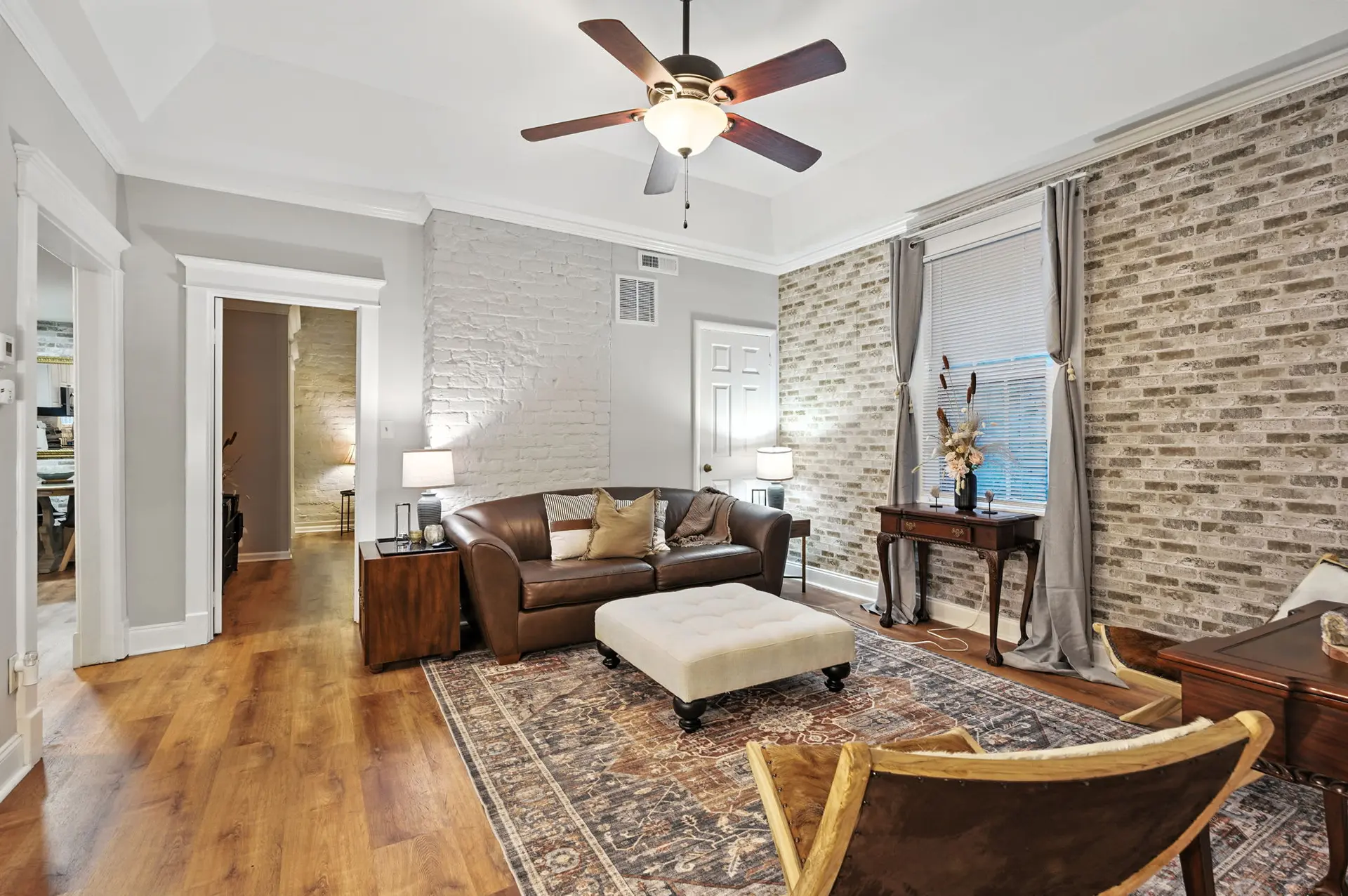 A living room with a brown leather sofa, an ottoman, and a ceiling fan.