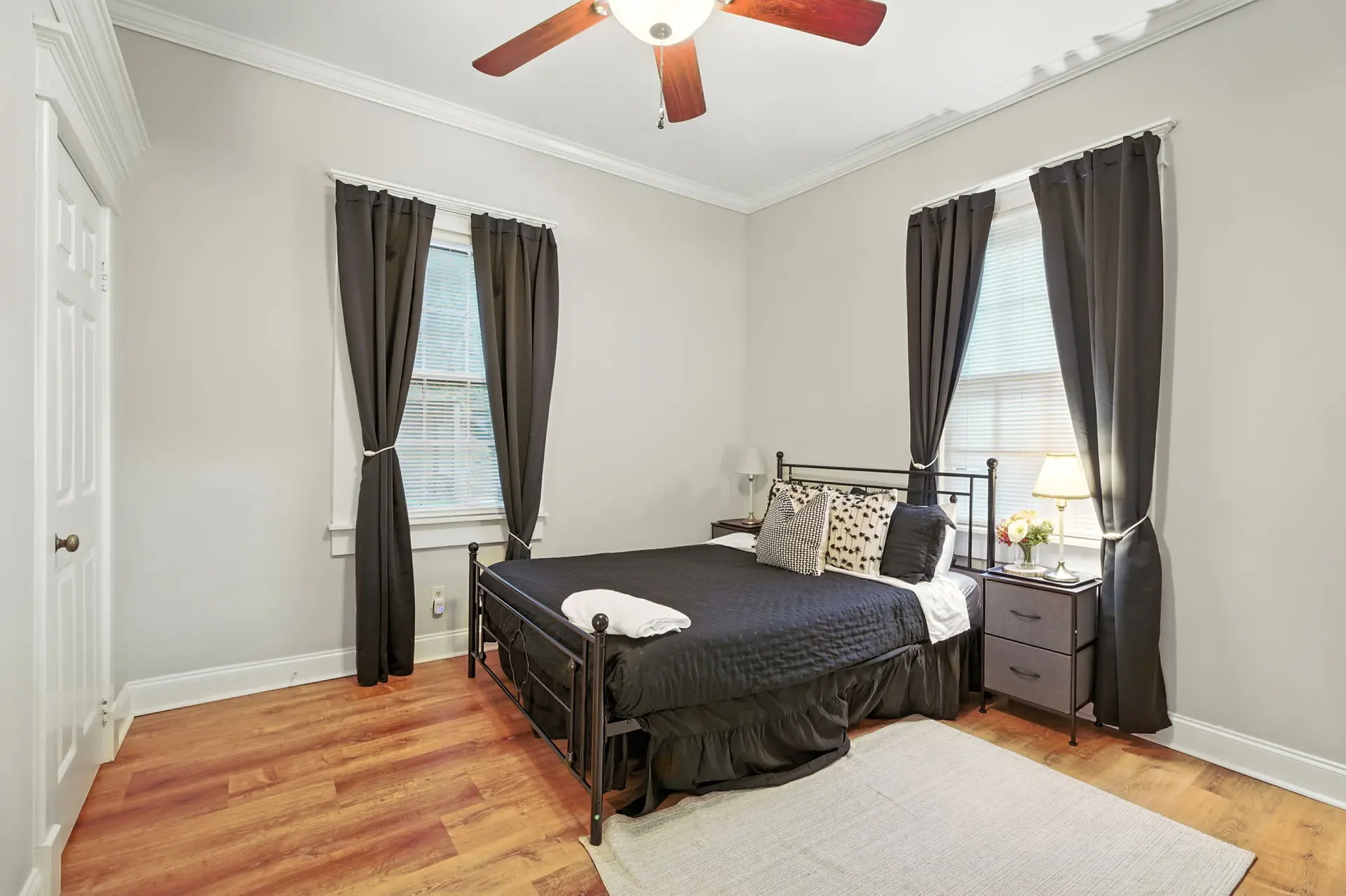 A black metal bed with a black comforter and decorative pillows sits on a wood floor.