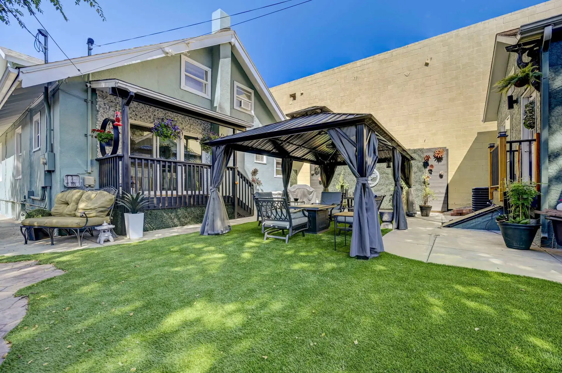 A backyard patio with a gazebo and outdoor furniture sits on artificial grass.