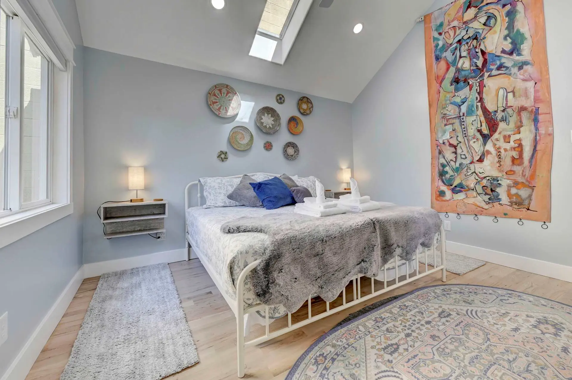 Bedroom with a white bed, a large colorful tapestry, and decorative wall plates.