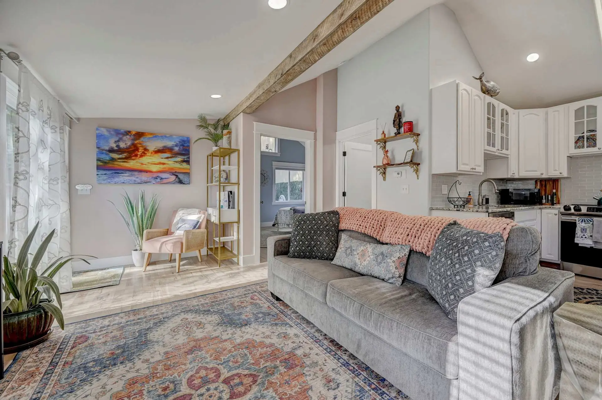 A living room with a gray sofa, patterned rug, and open doorway to a kitchen.