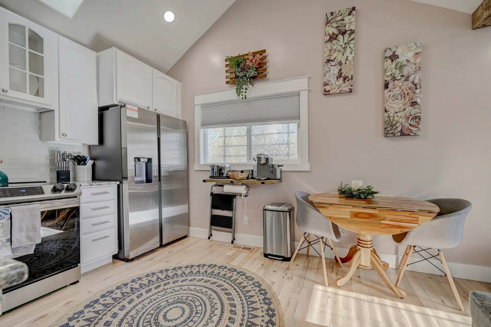 A cozy kitchen with a round rug, a small dining table, stainless steel appliances, and a window with