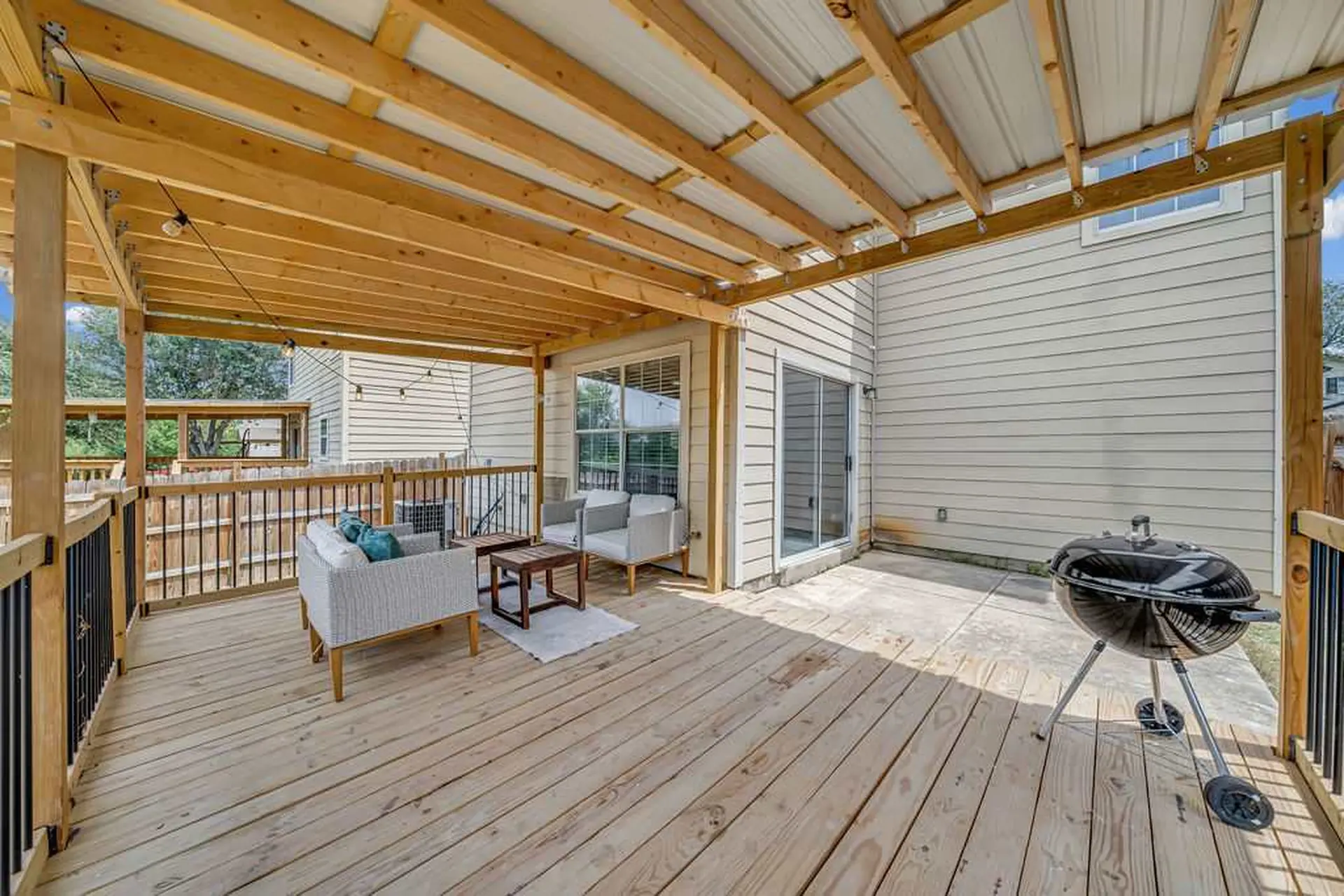 A wooden deck with a covered area, seating, and a grill.