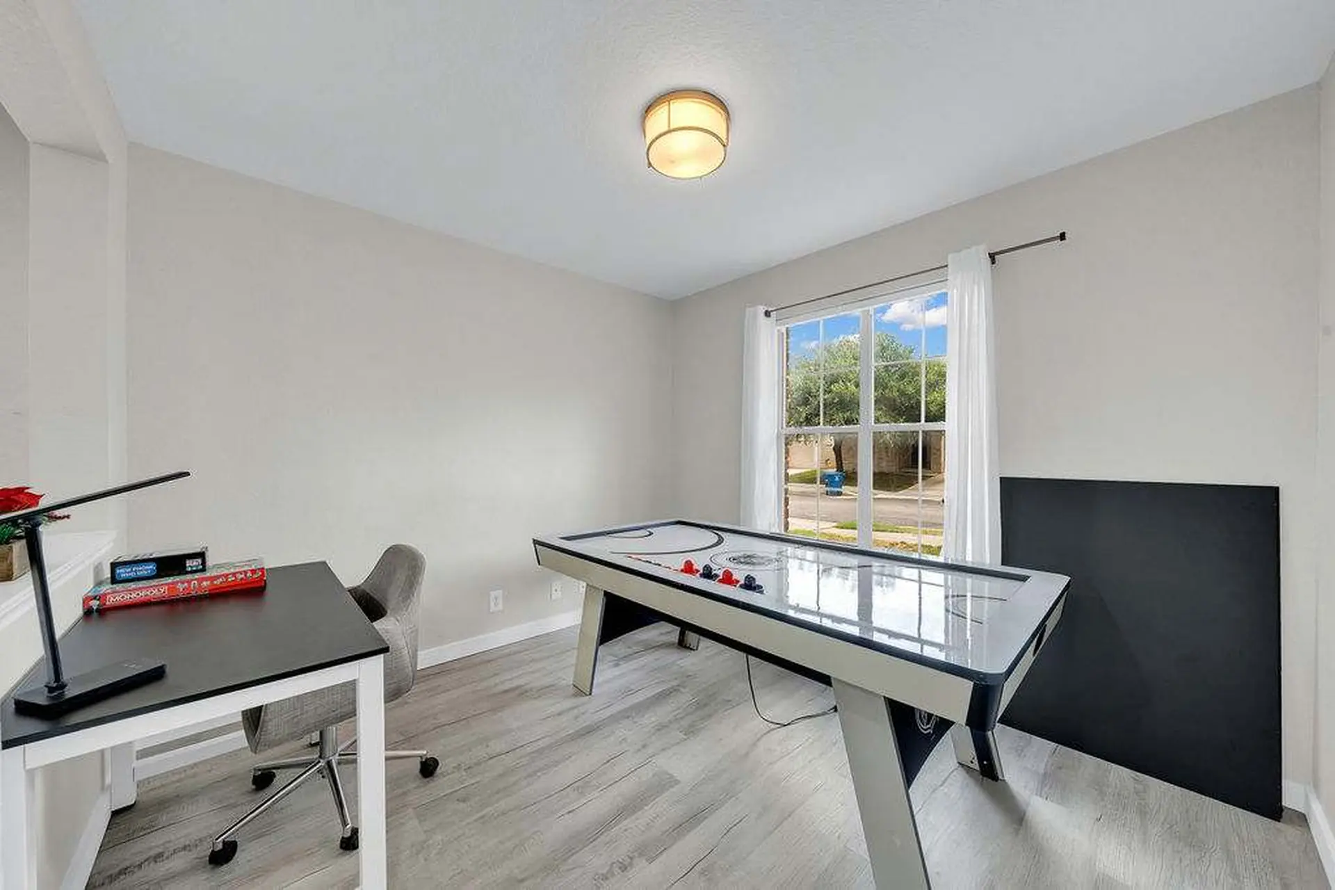 A desk with a lamp and games is next to an air hockey table and a large black board.