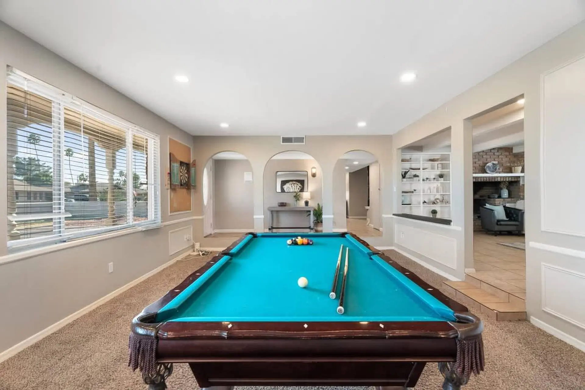 A pool table with a blue felt, set in a room with arched doorways and a fireplace.