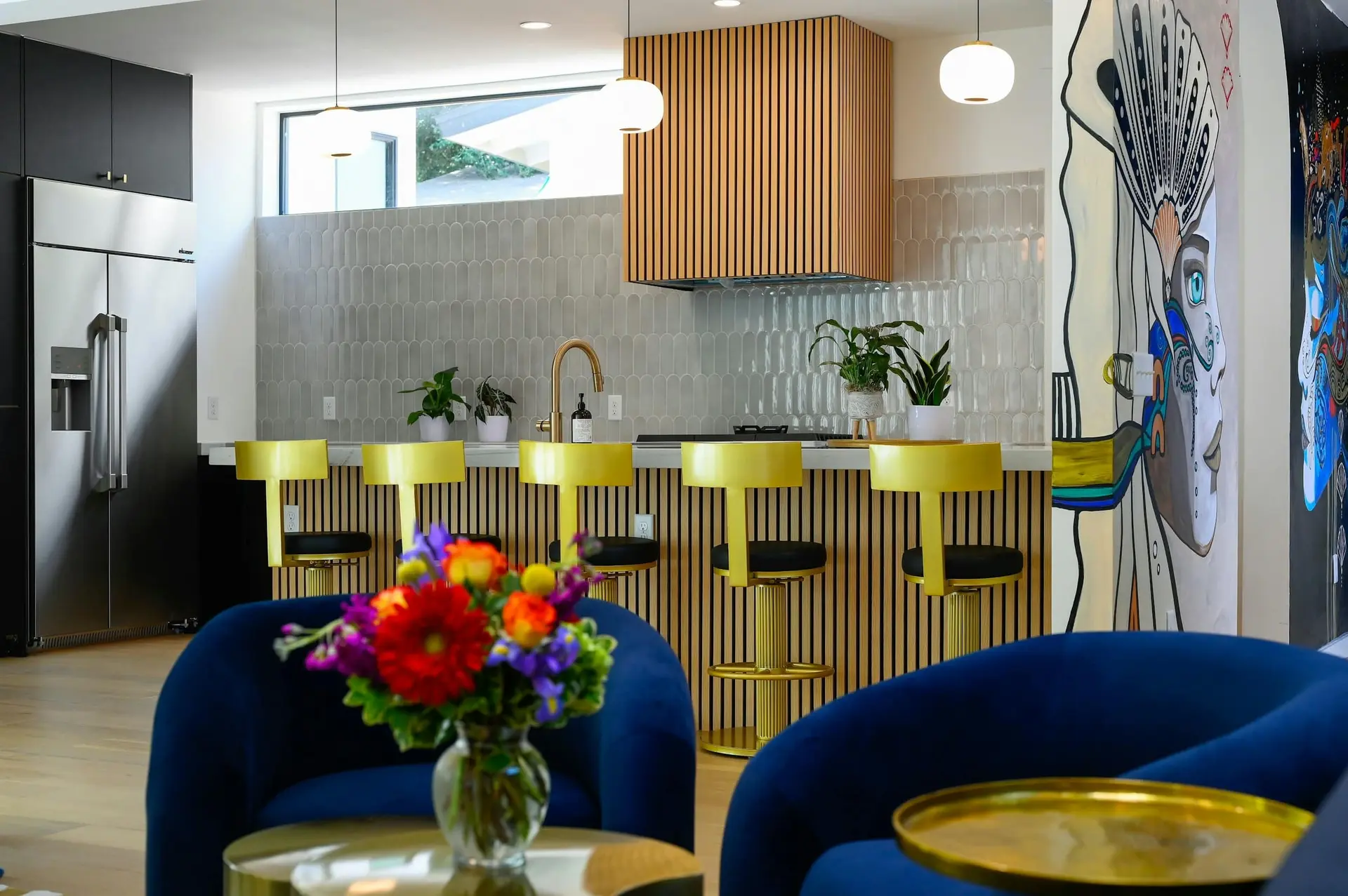 A stylish kitchen with yellow bar stools, a modern hood, and bold artwork on the wall.