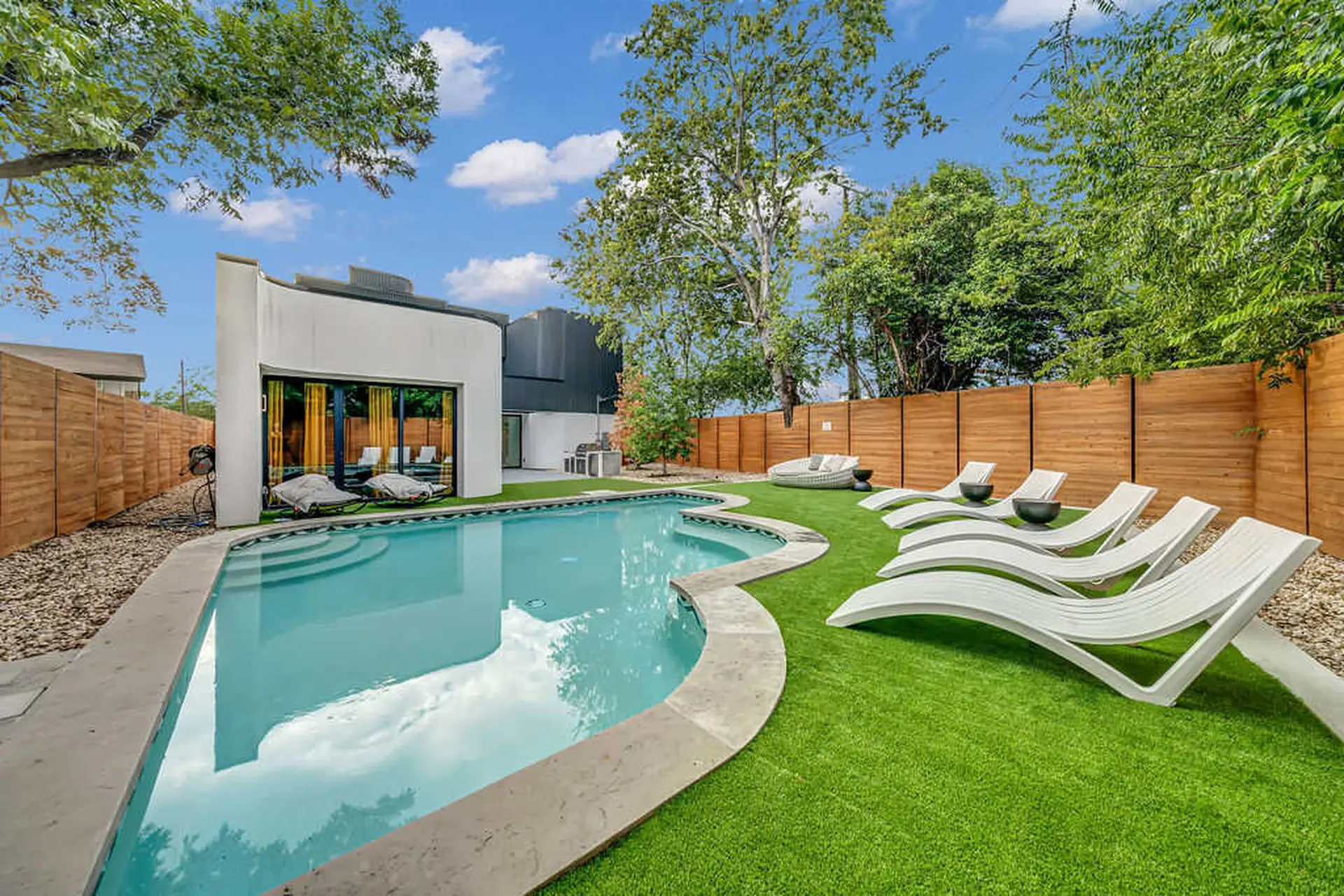 Modern backyard with a pool, lounge chairs, and a wooden fence.