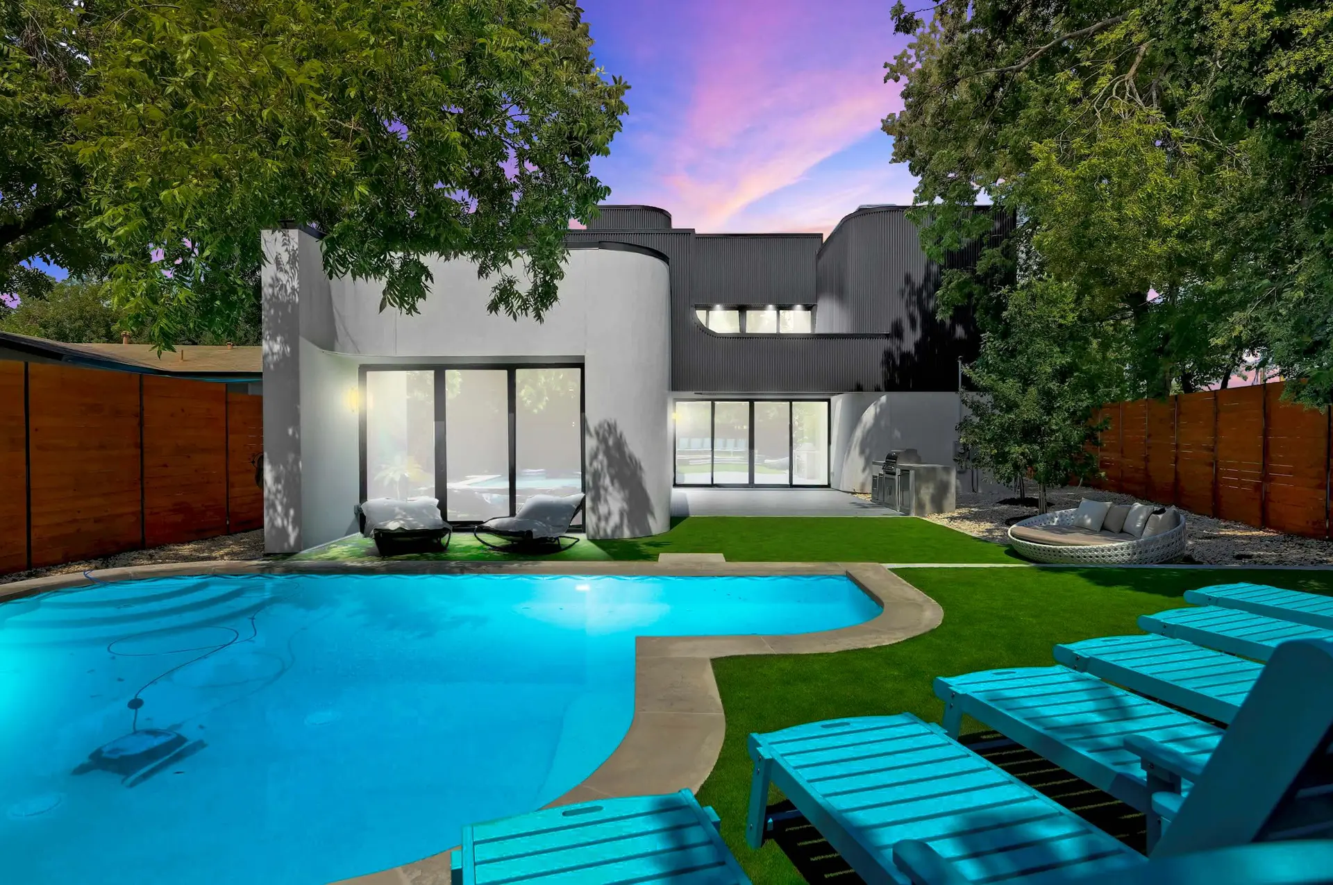 Modern home with pool and lounge chairs, at sunset.