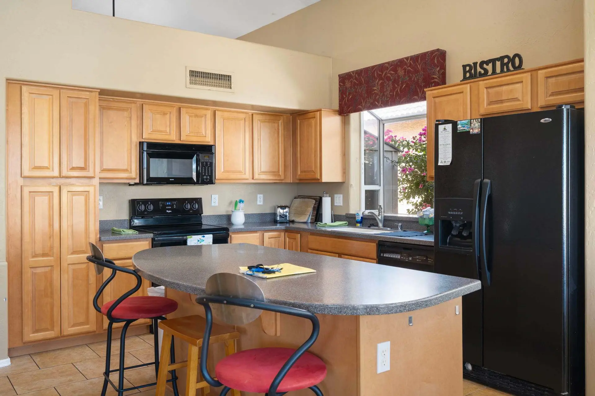 Kitchen with light wood cabinets, black appliances, and a kitchen island with bar stools.