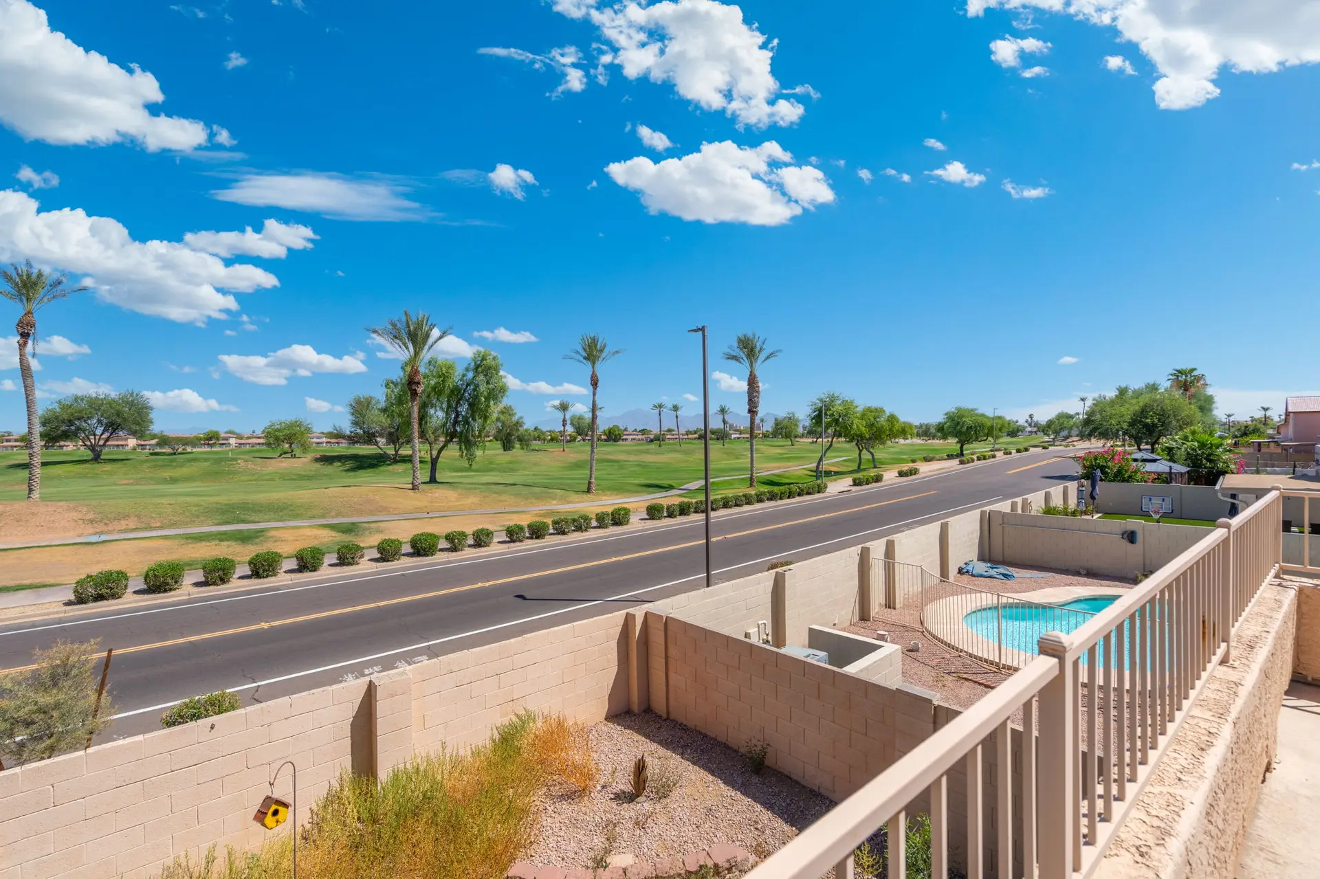 A view of a road, golf course, and swimming pool on a sunny day.