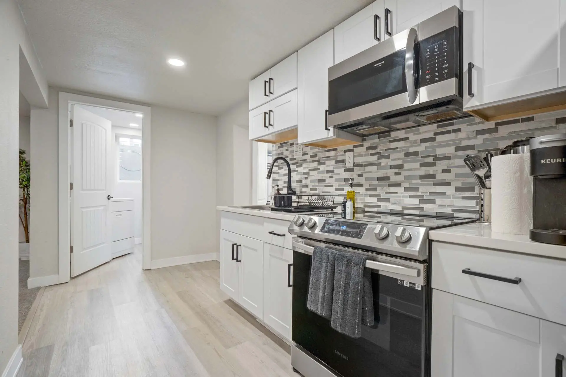 A modern kitchen with white cabinets, stainless steel appliances, and a sleek tiled backsplash.