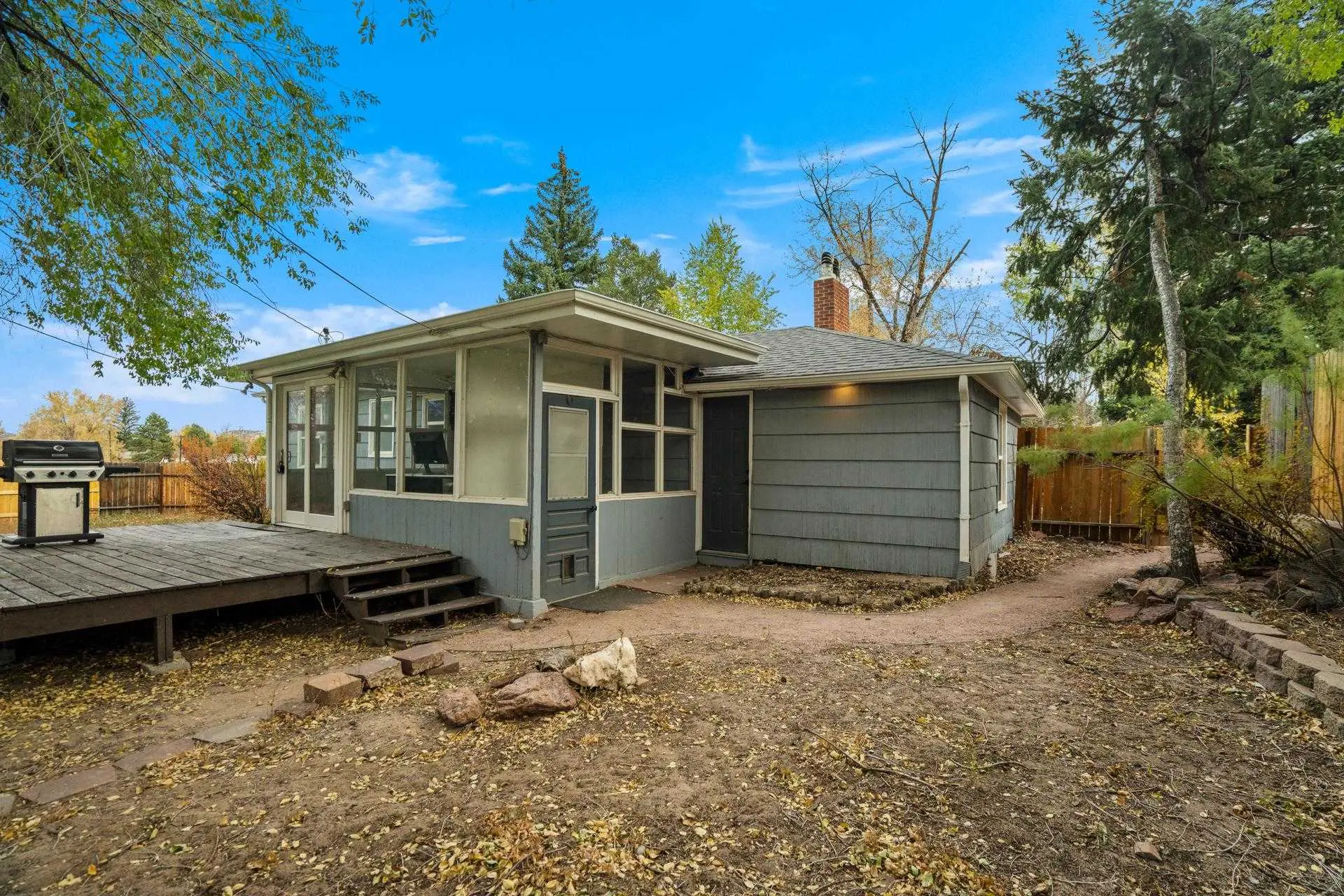A grey house with a sunroom and a deck with a grill.