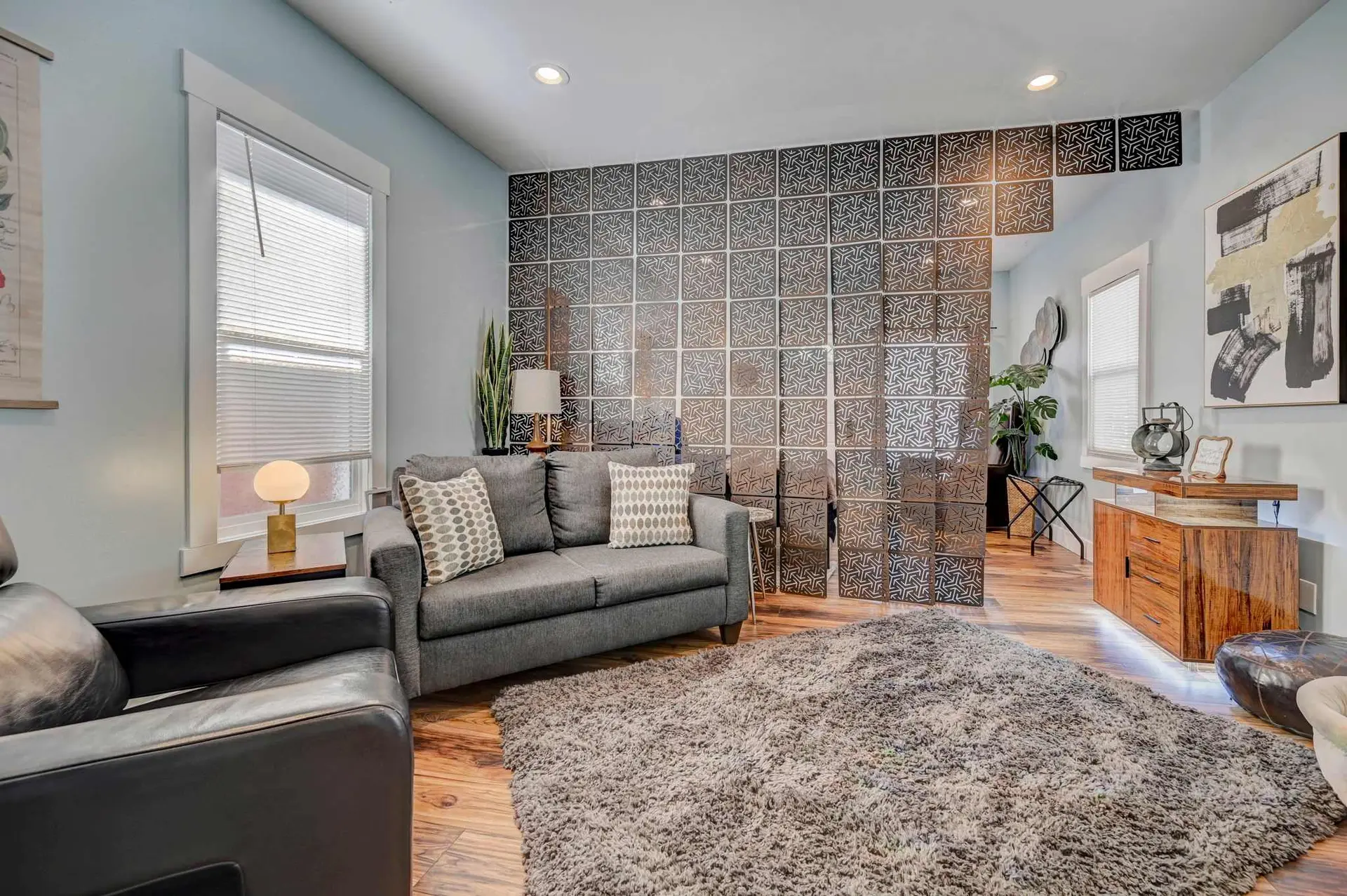 A modern living room with a gray sofa, black leather armchair, patterned screen, and wooden furnitur