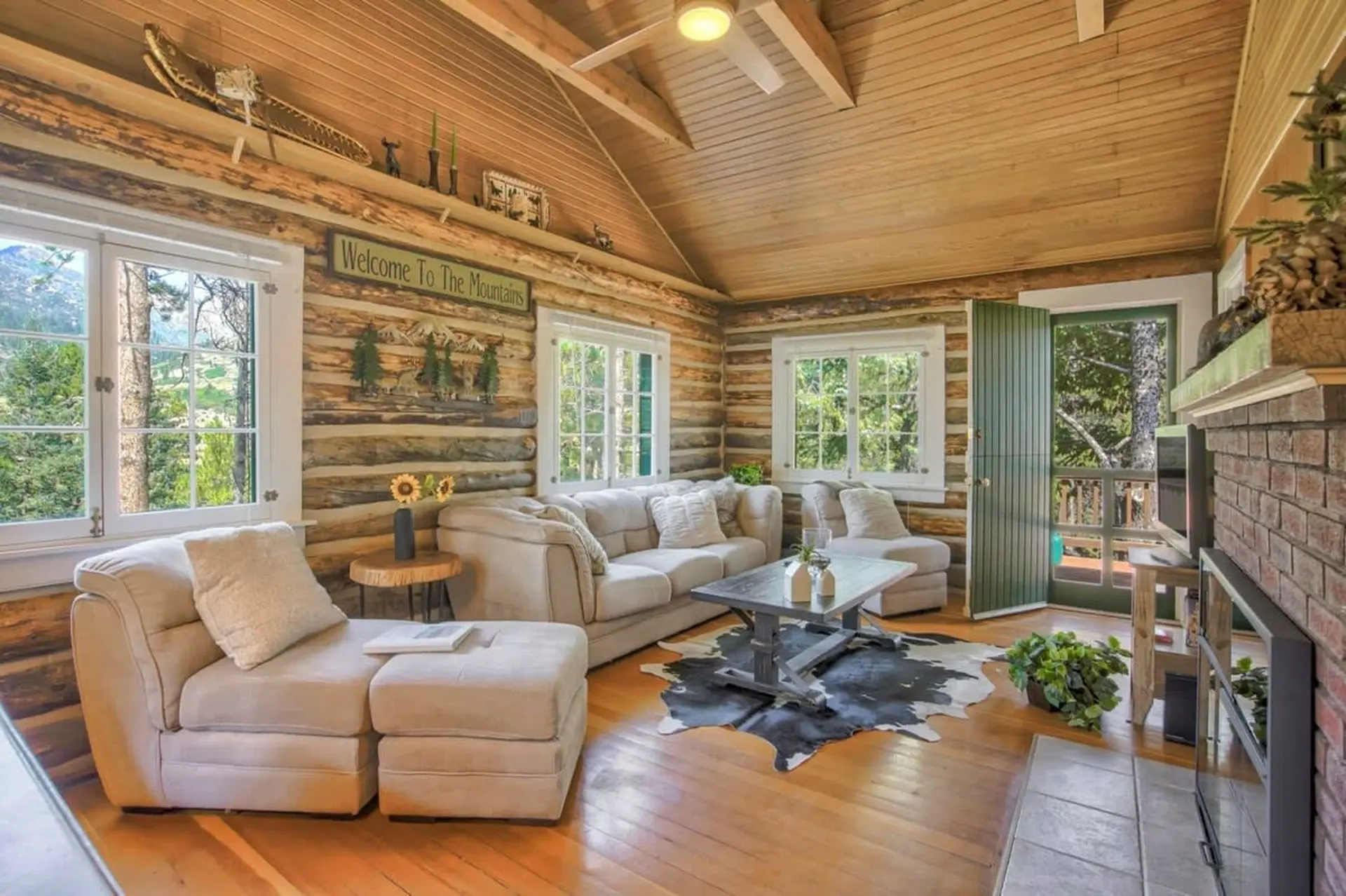Cozy log cabin living room with a stone fireplace, comfortable sectional, and large windows.