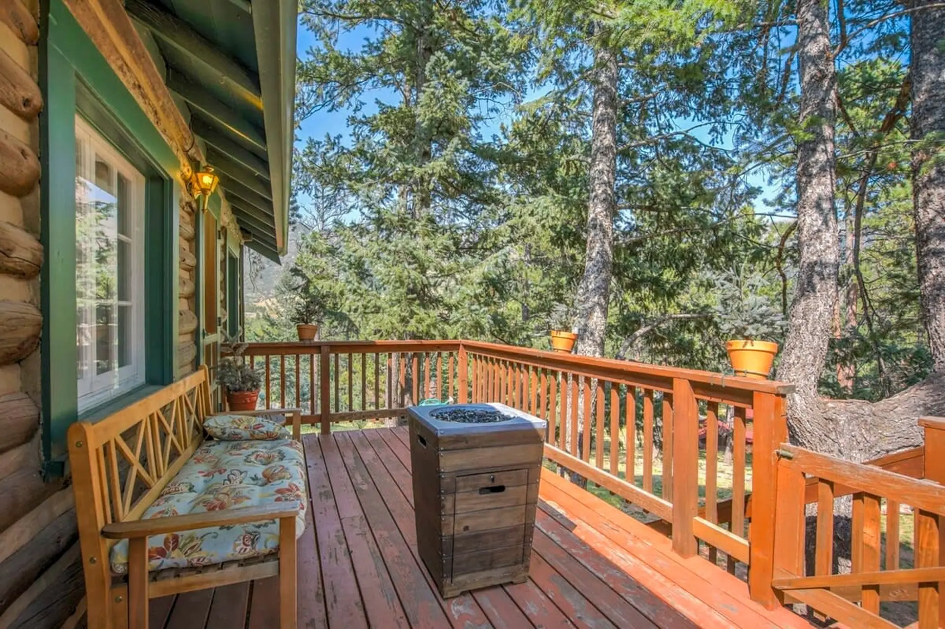 A wooden deck with a bench, fire pit, and railings overlooks a forest.