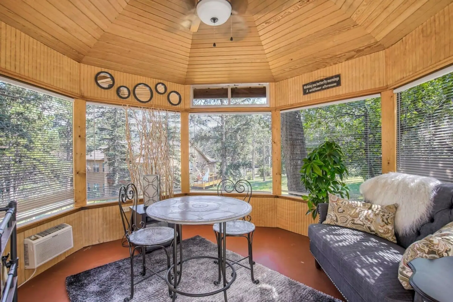 A sunroom with a round table and chairs, a couch, and large windows overlooking a wooded area.