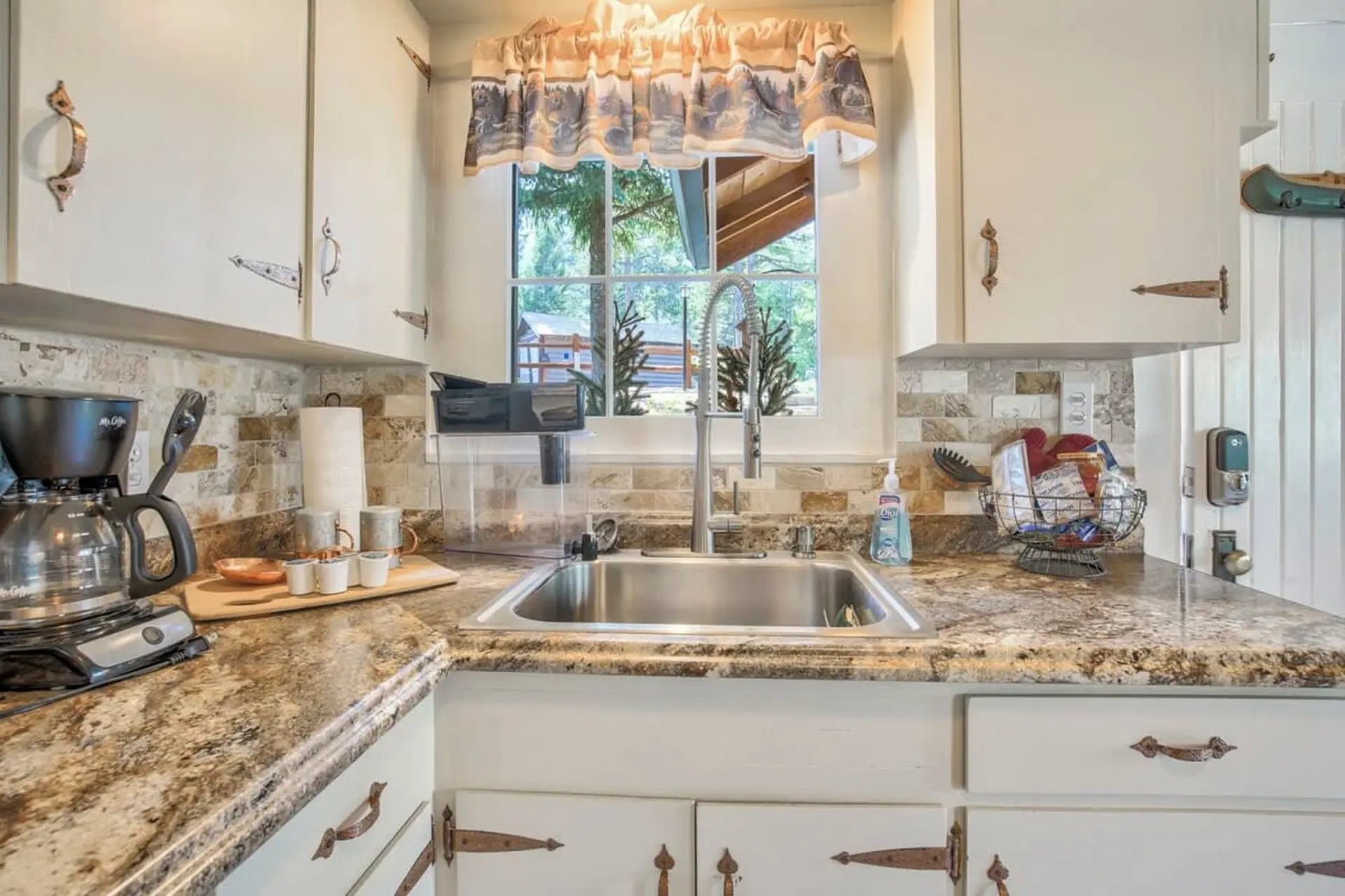 Kitchen counter with sink, coffee maker, and cabinets with rustic hardware.