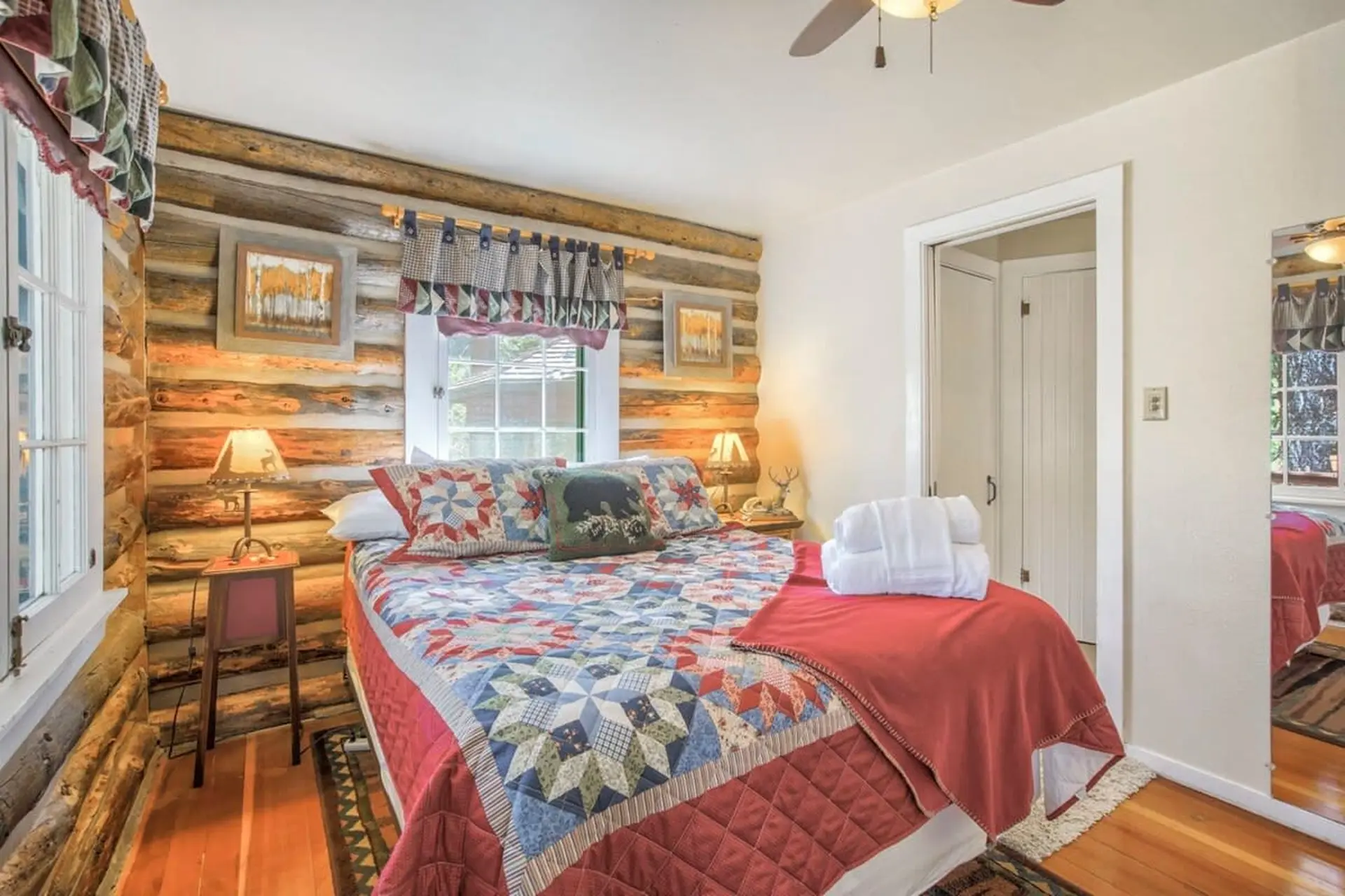 A cozy bedroom with a log-cabin theme, featuring a quilted bed, rustic decor, and a ceiling fan.