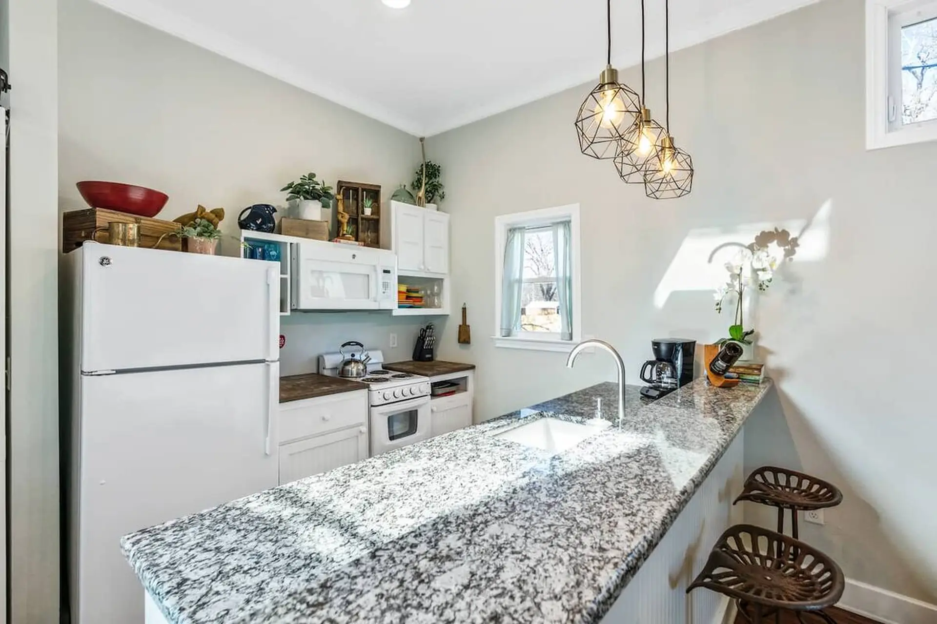 A modern kitchen features a white refrigerator, a white stove, and a granite countertop with a sink.