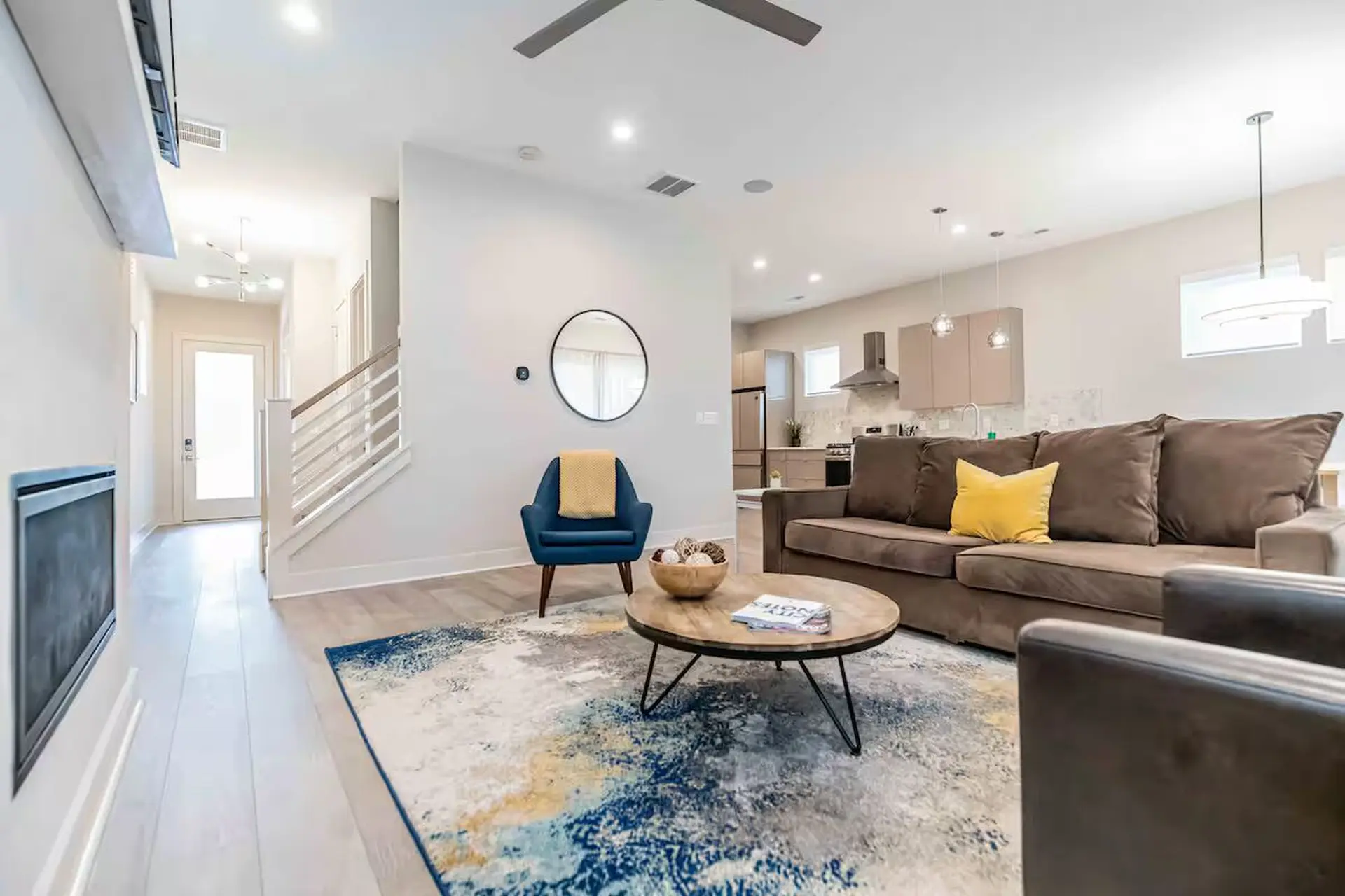 A living room with a brown couch, blue armchair, coffee table, and abstract rug.