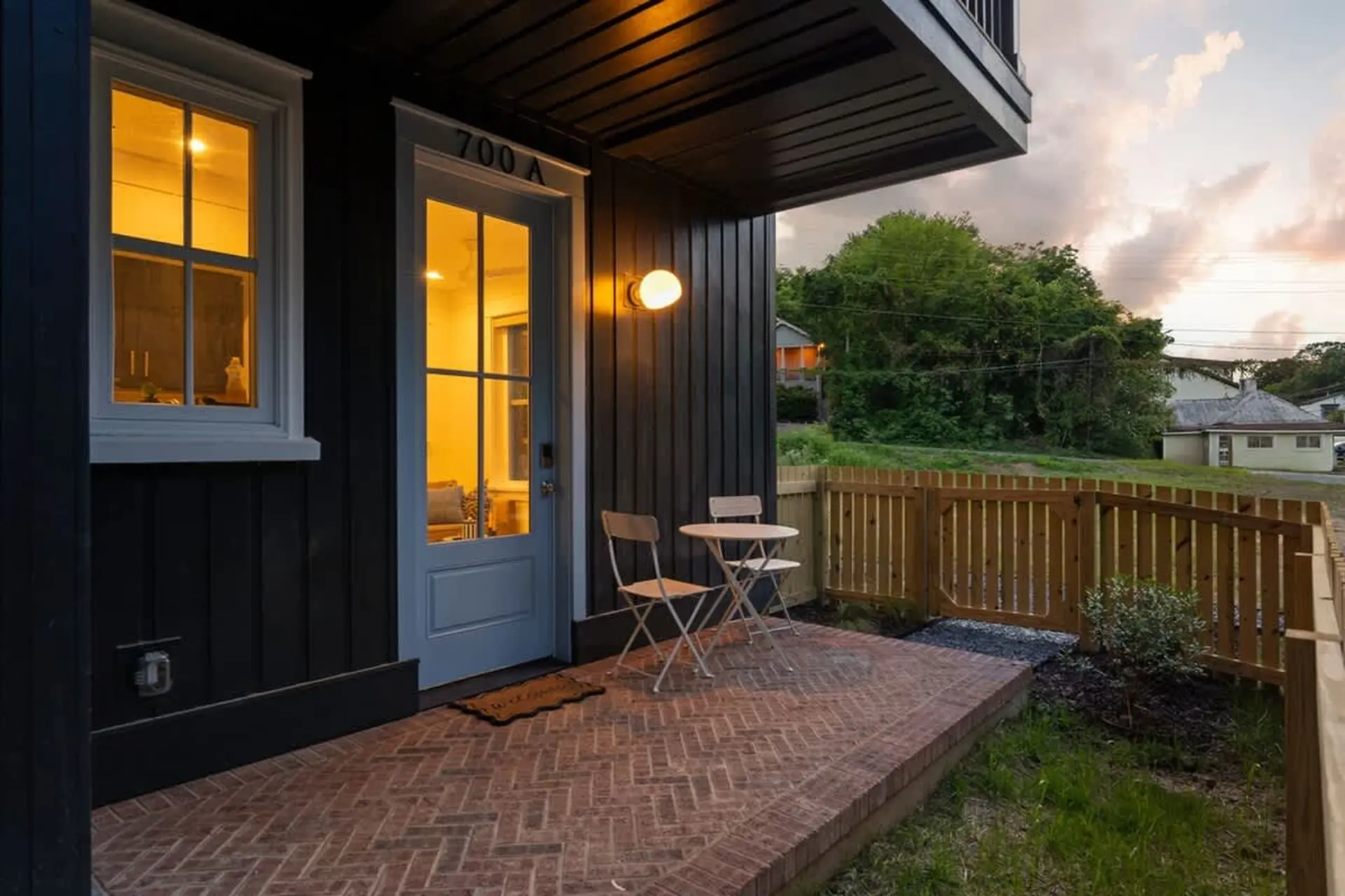 Small outdoor patio with a door, window, two chairs, and a table in front of a wooden fence.