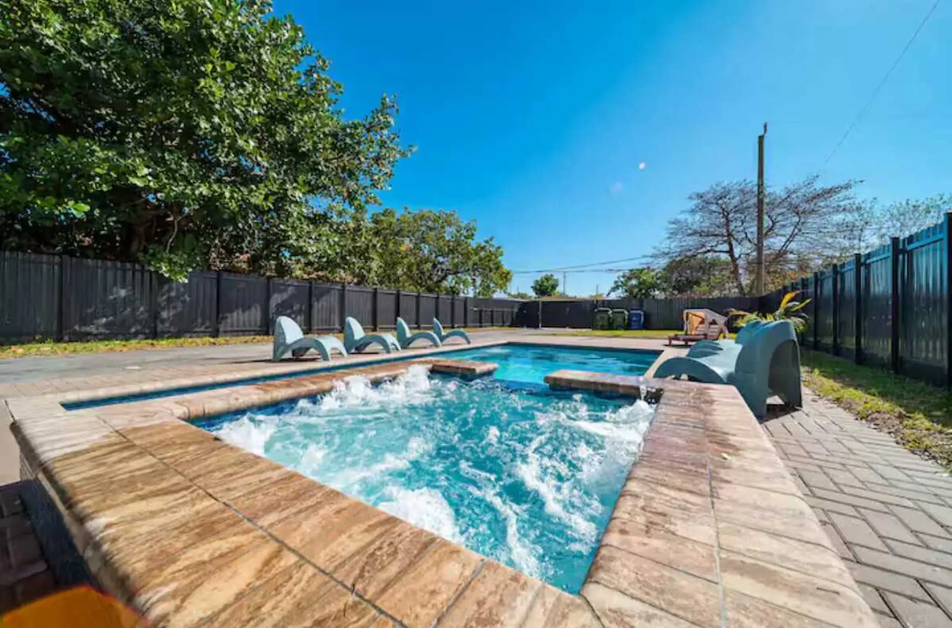 A sunny day at a backyard pool with a hot tub and lounge chairs.