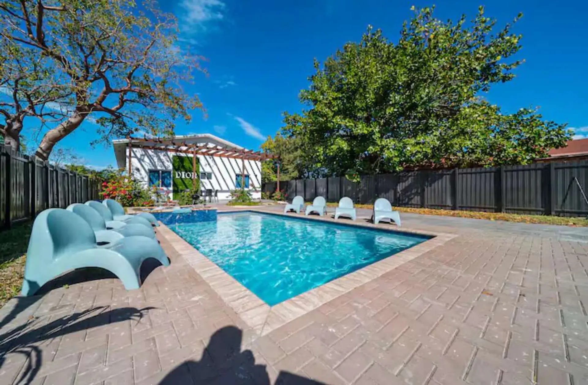 A backyard pool area with lounge chairs, white chairs, and a building with "DIOR" on it.