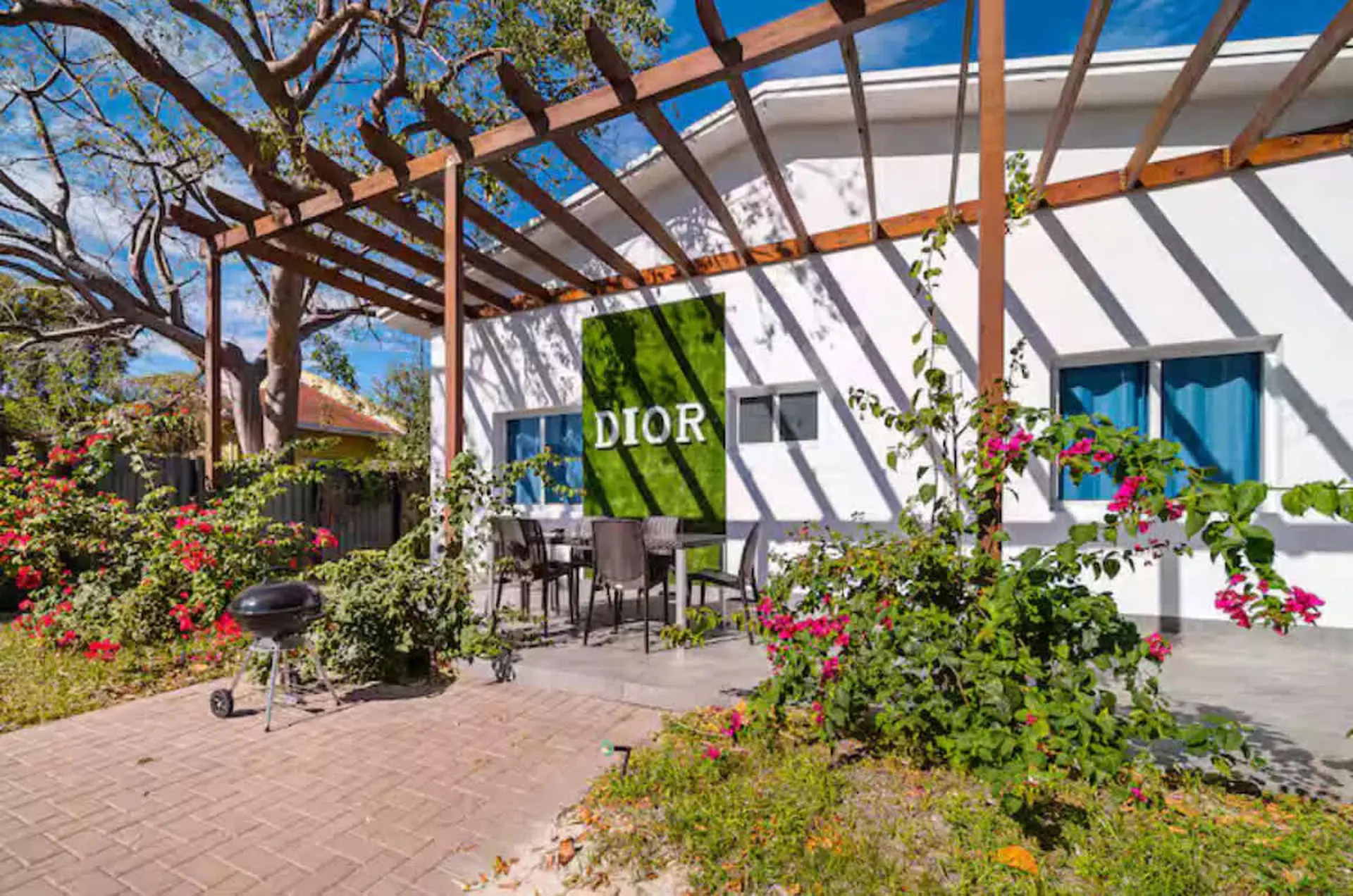 A white building with a green DIOR sign, a patio with chairs and a grill, and lush greenery.