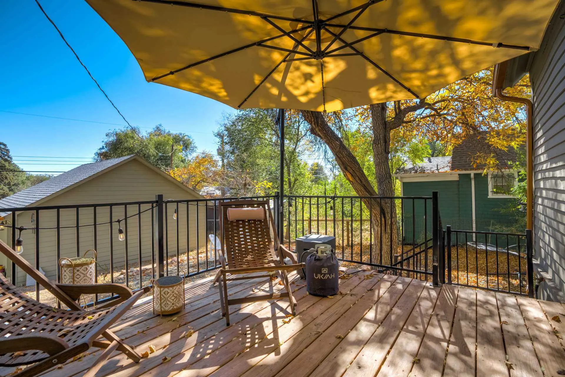 Deck with chairs, umbrella, and propane tank, overlooking a yard in autumn.