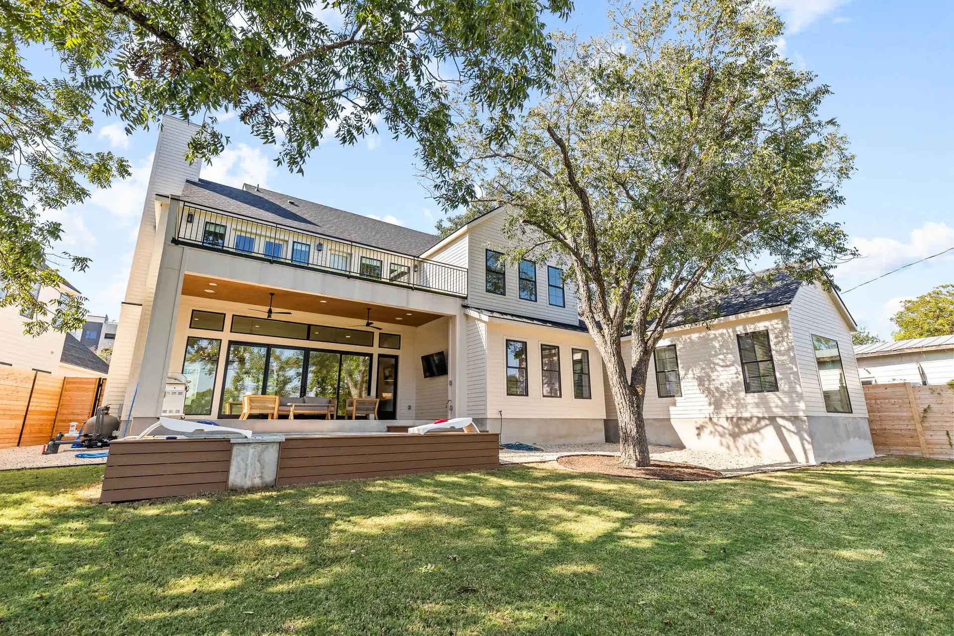 A modern home with a balcony and large windows overlooks a lush green lawn.