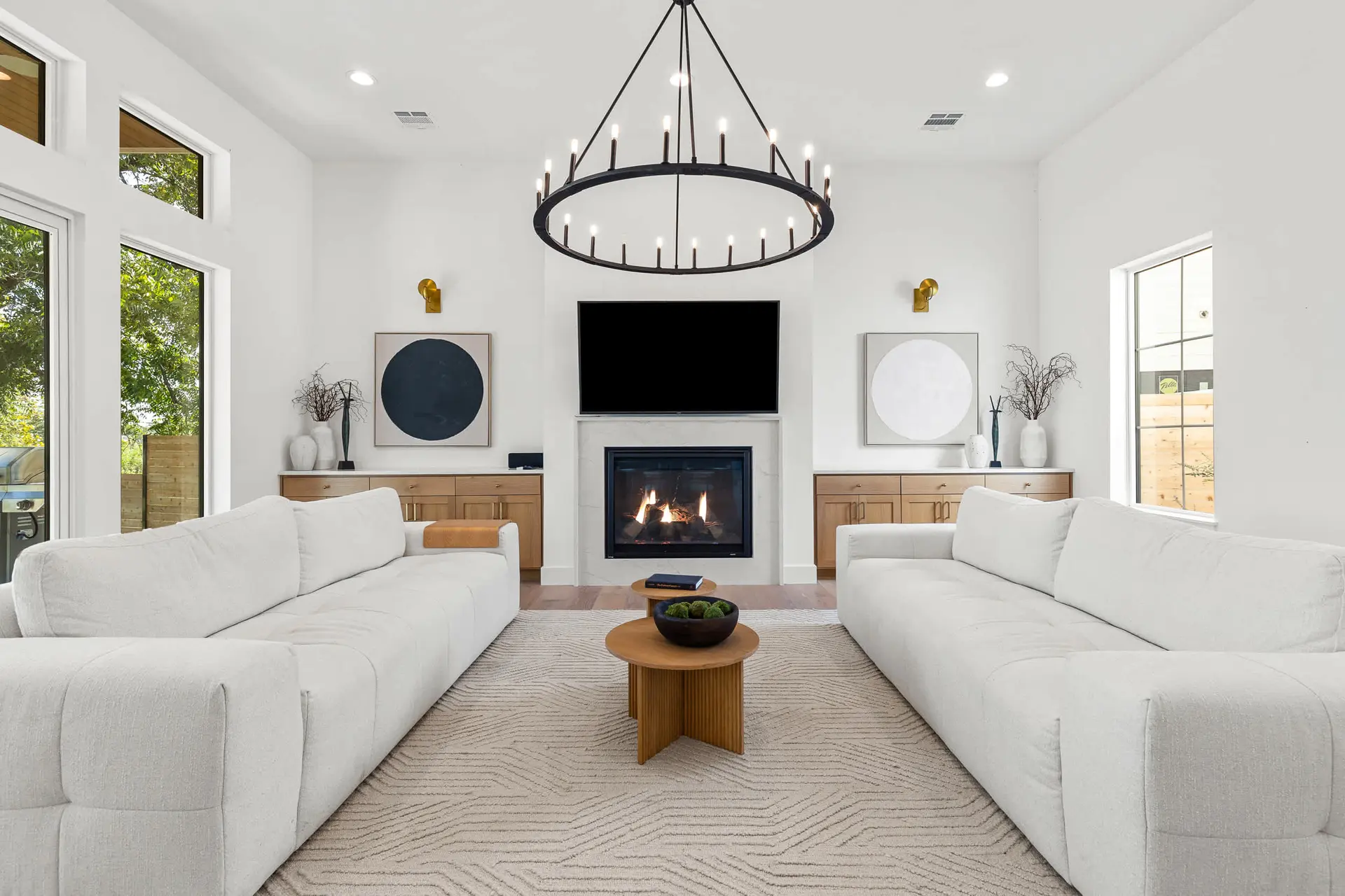A bright living room with two white sofas facing each other, a fireplace, and a large chandelier.