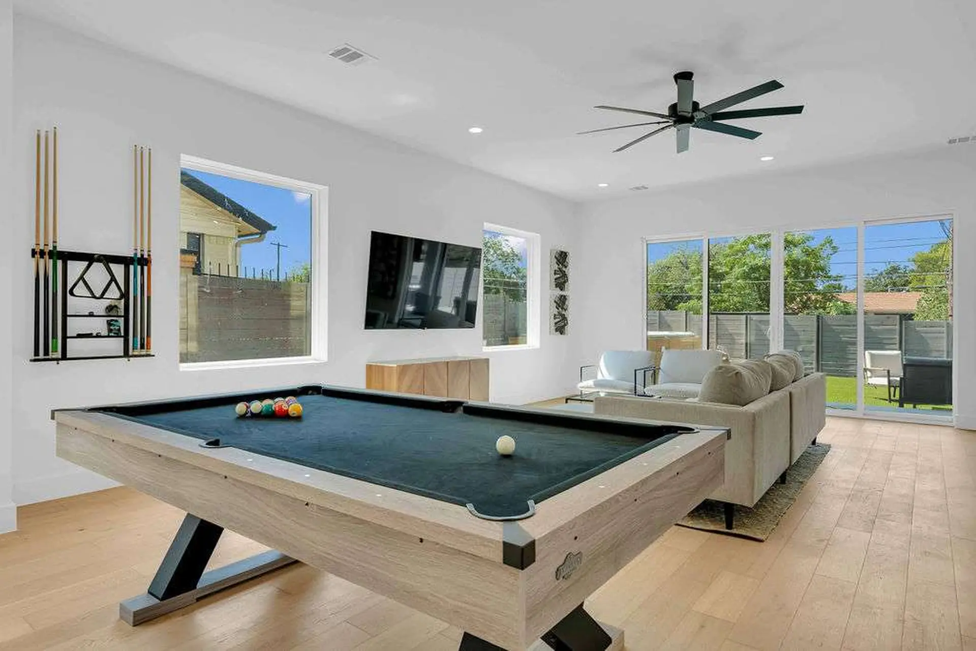 A modern living room with a pool table, sectional sofa, and large windows.
