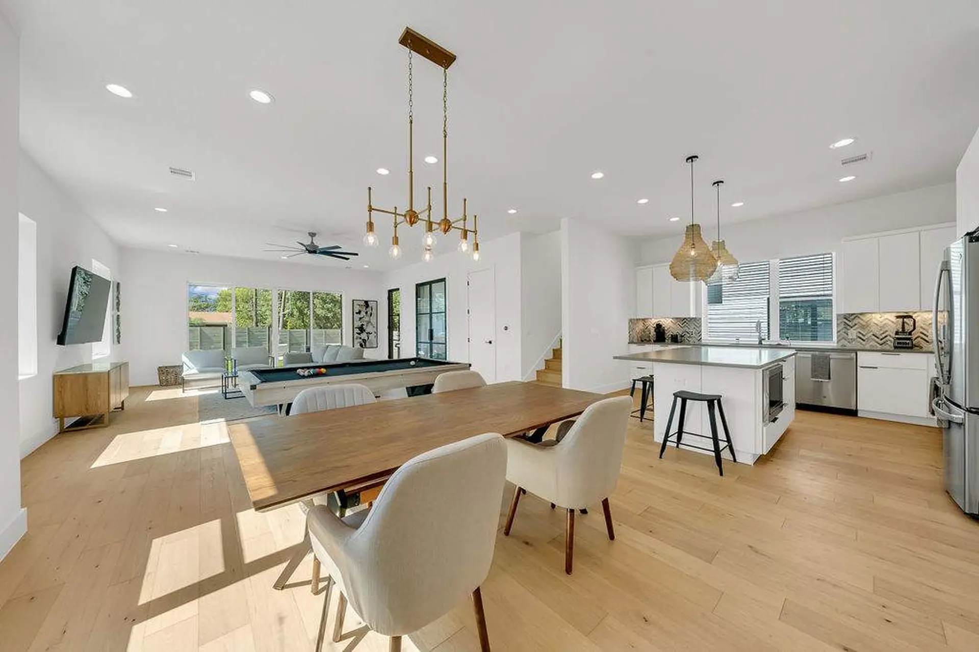 A dining table with chairs is in front of a kitchen island with stools.