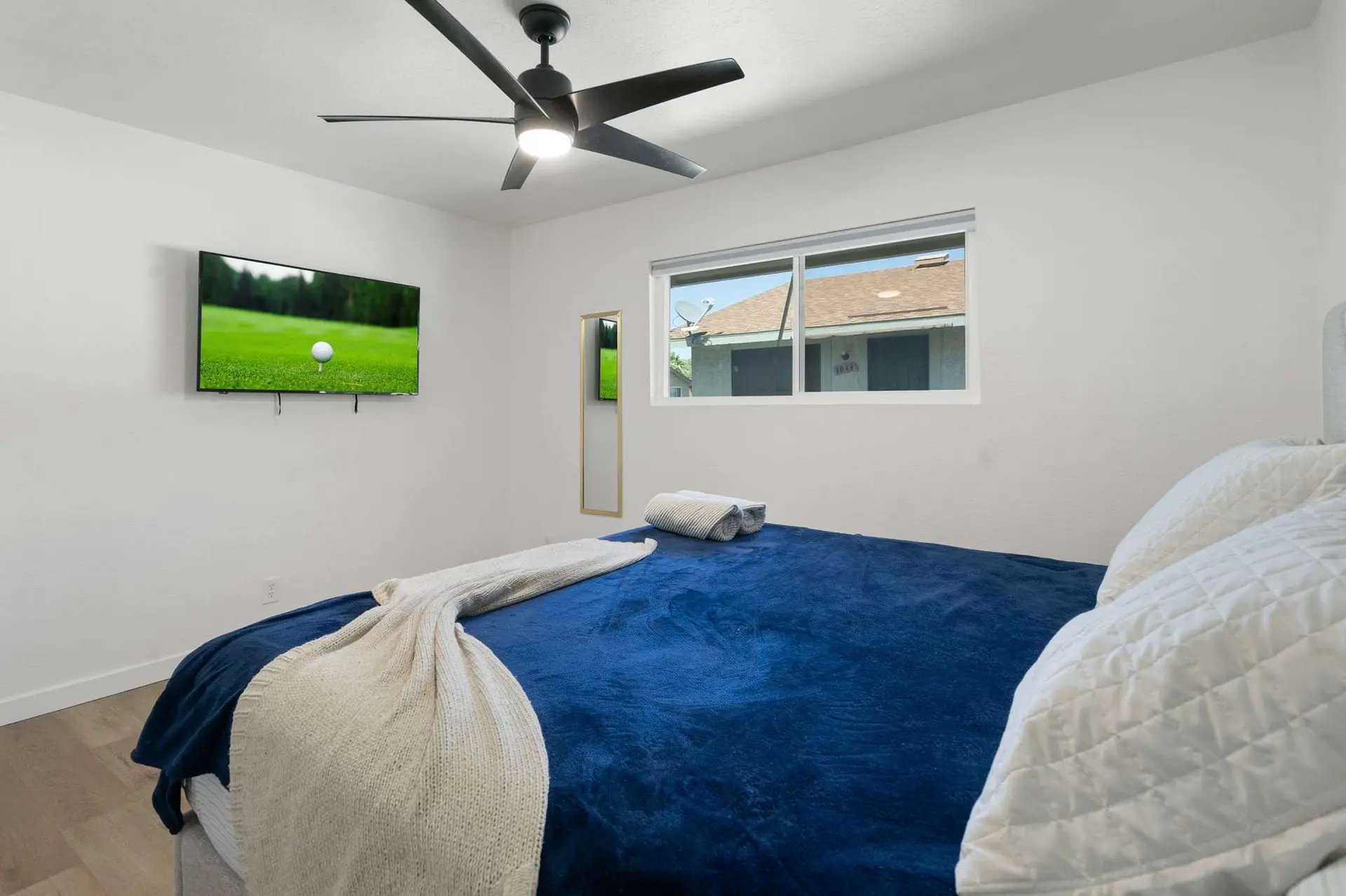 A bedroom with a bed, a TV, a ceiling fan, and a window.