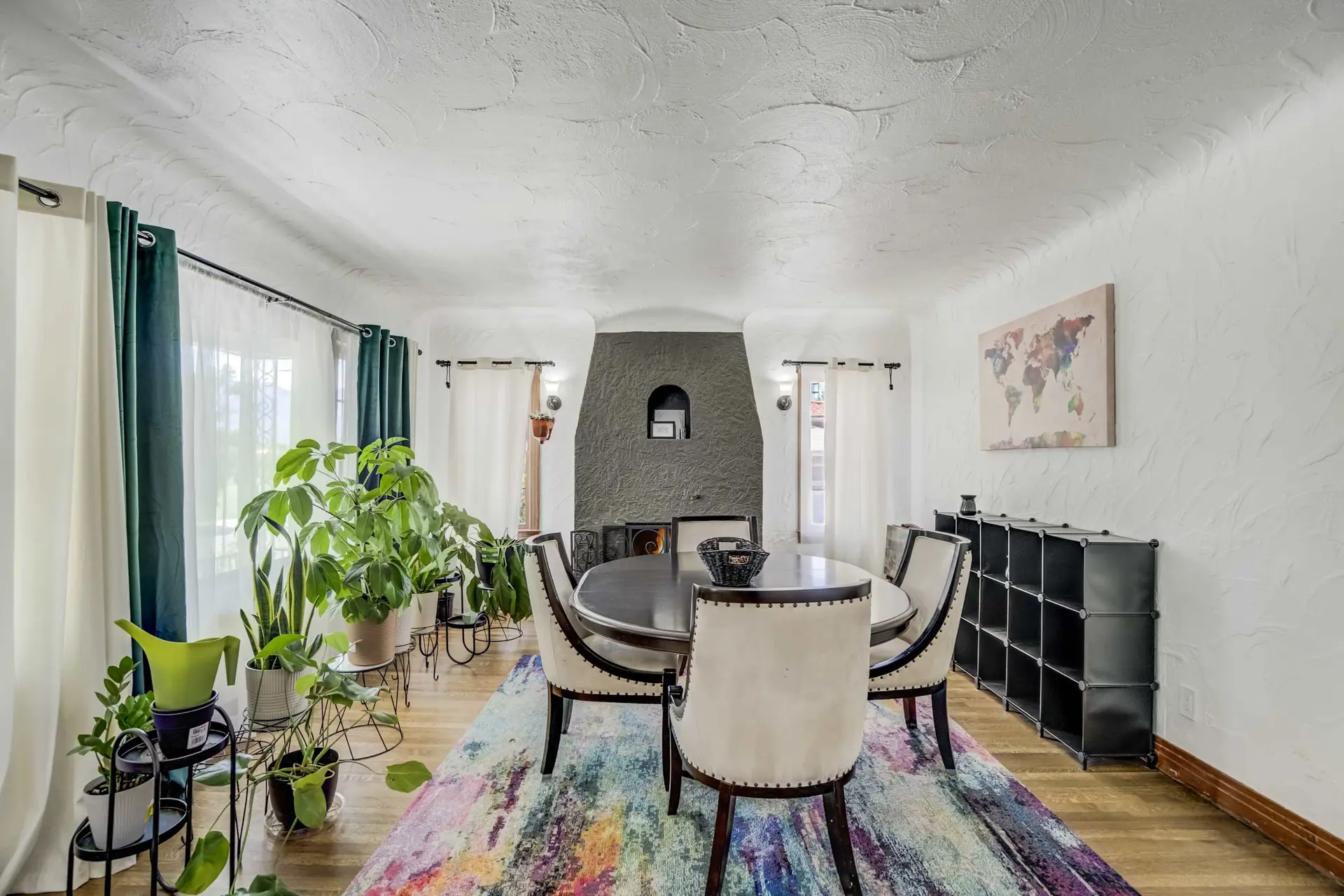 Dining room with a round table, chairs, fireplace, and plants.
