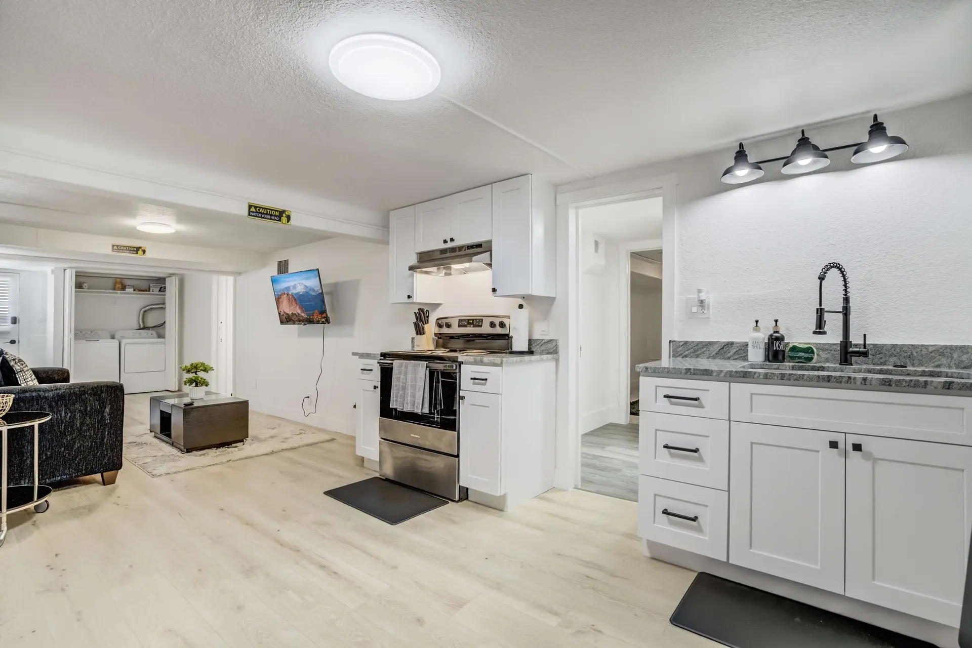 A bright, modern kitchen and living area with white cabinets, a stainless steel stove, and a mounted
