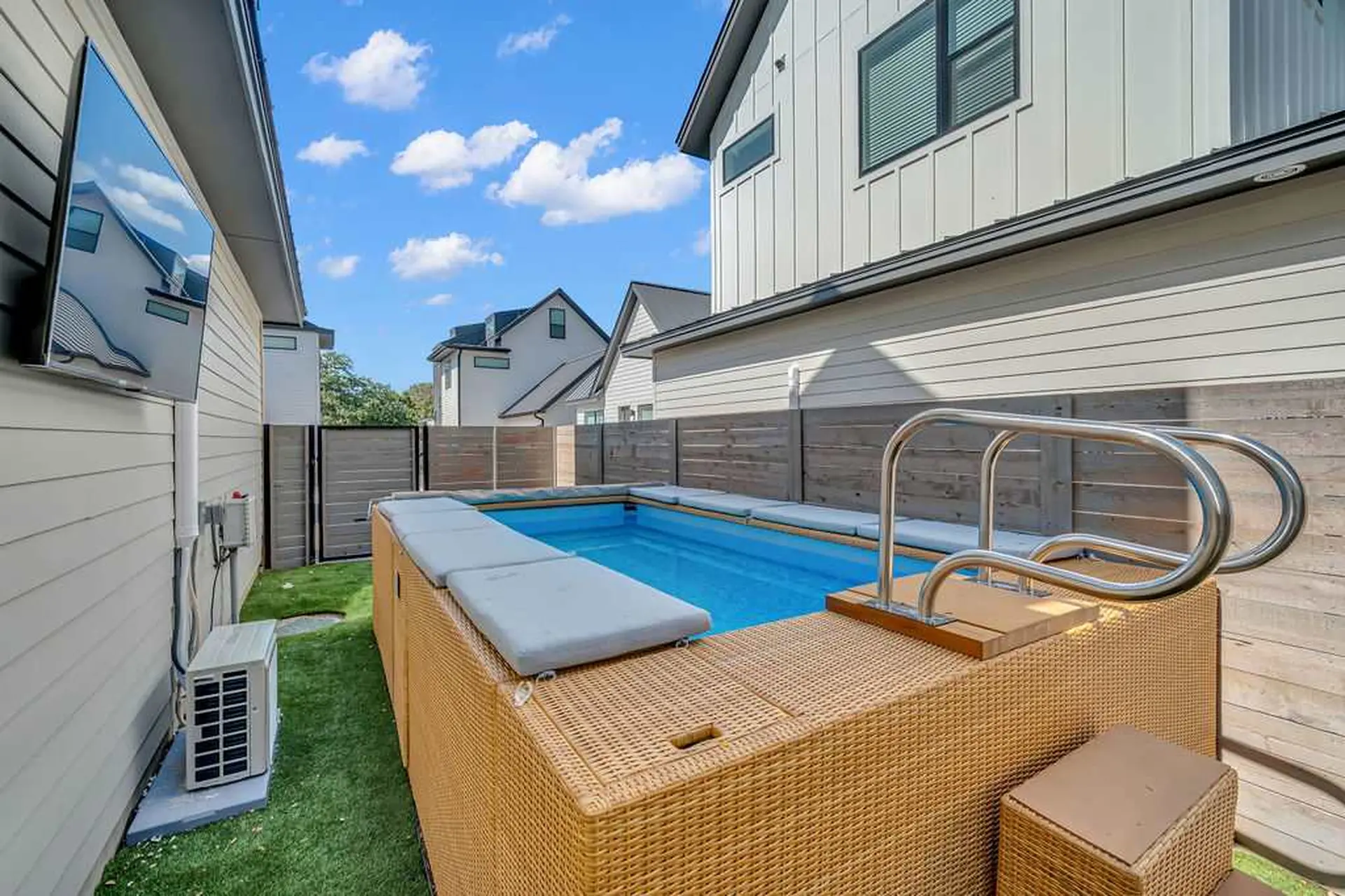 An outdoor pool with a modern home and a TV mounted on the side of the house.