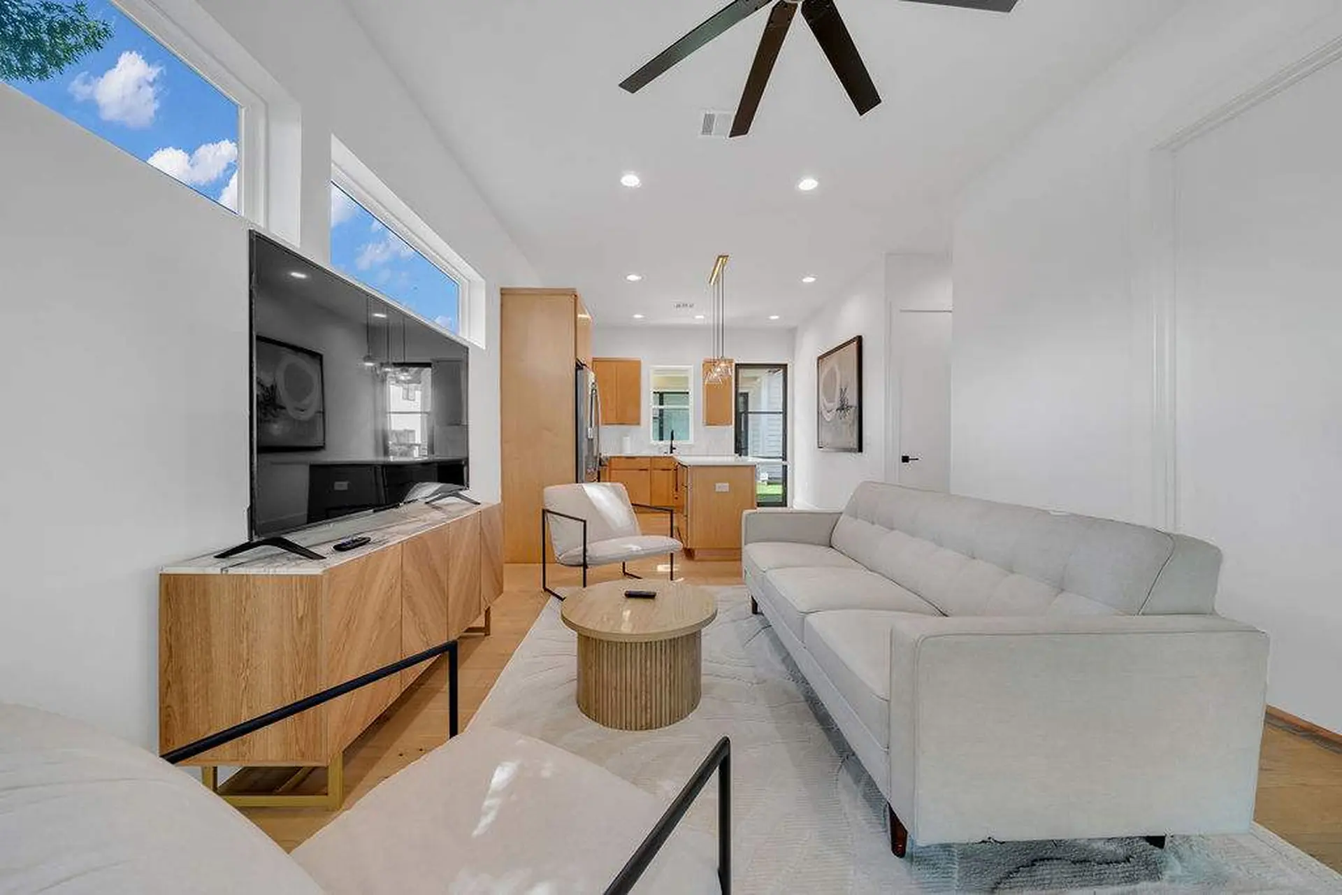 A **modern living room** with a **large white sofa**, **tv on a wooden cabinet**, and **kitchen in t