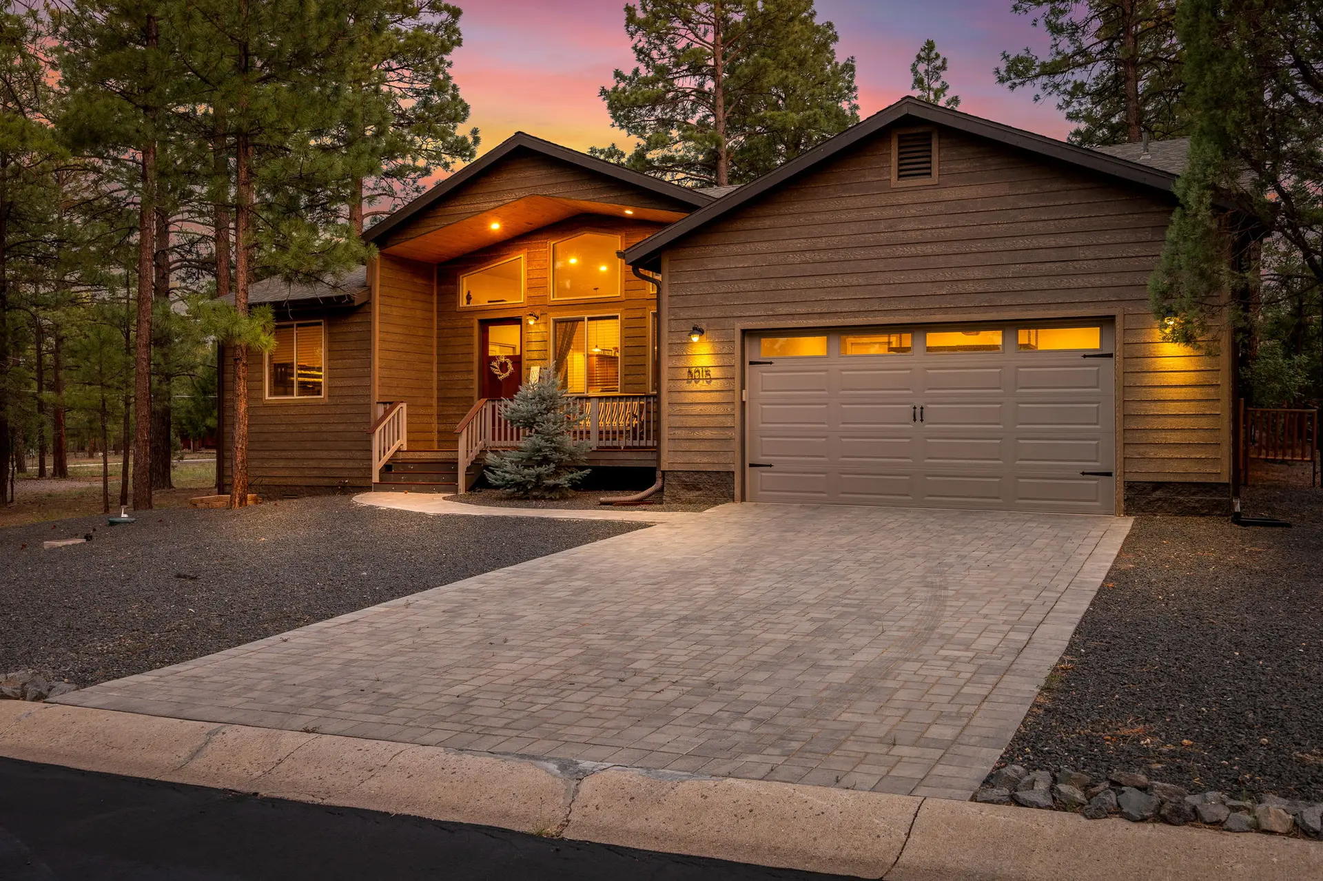 A modern wood-sided house with a garage and driveway at sunset.